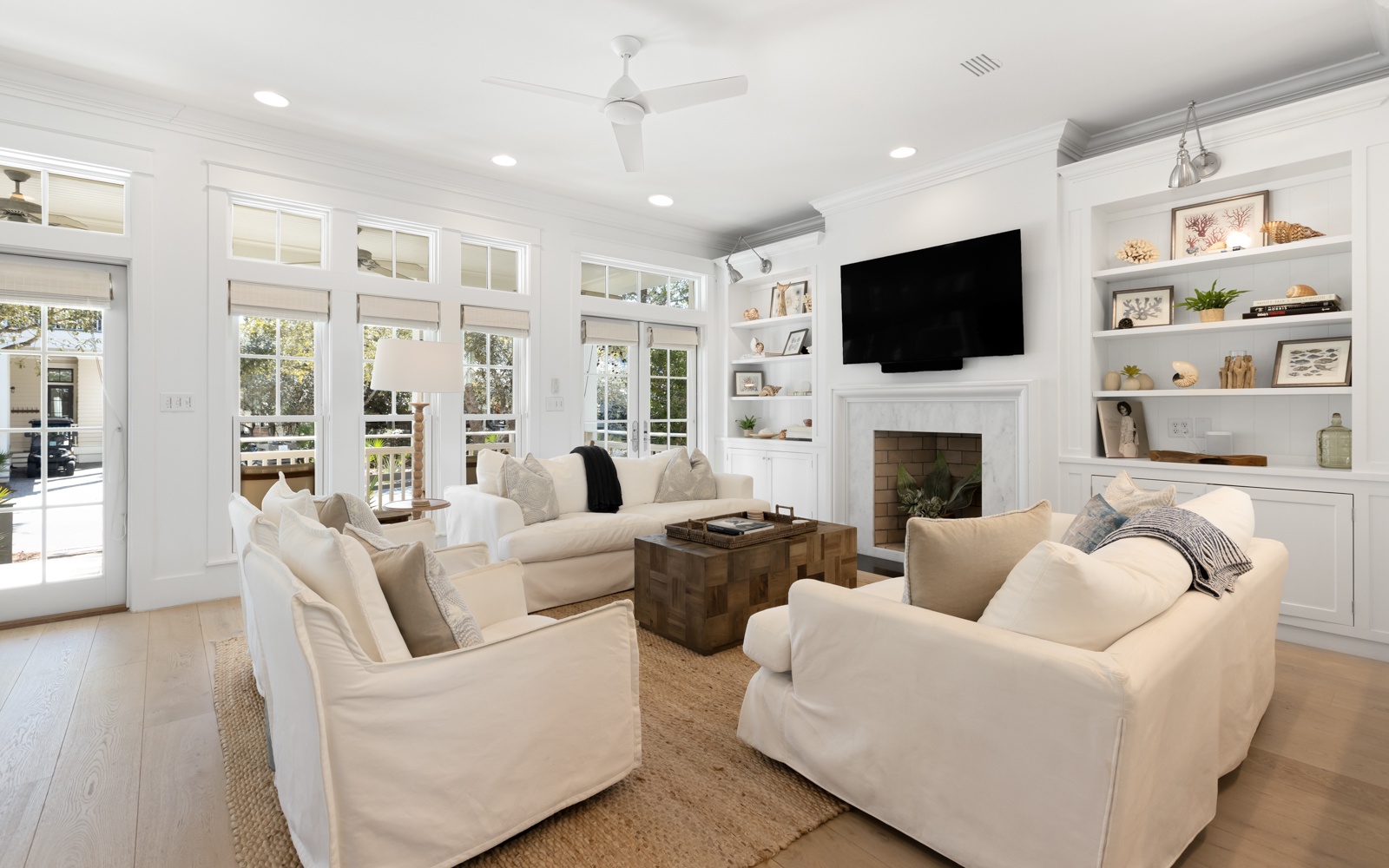 Sink into plush white sofas by the fireplace where natural light floods through elegant French doors, creating your perfect retreat.