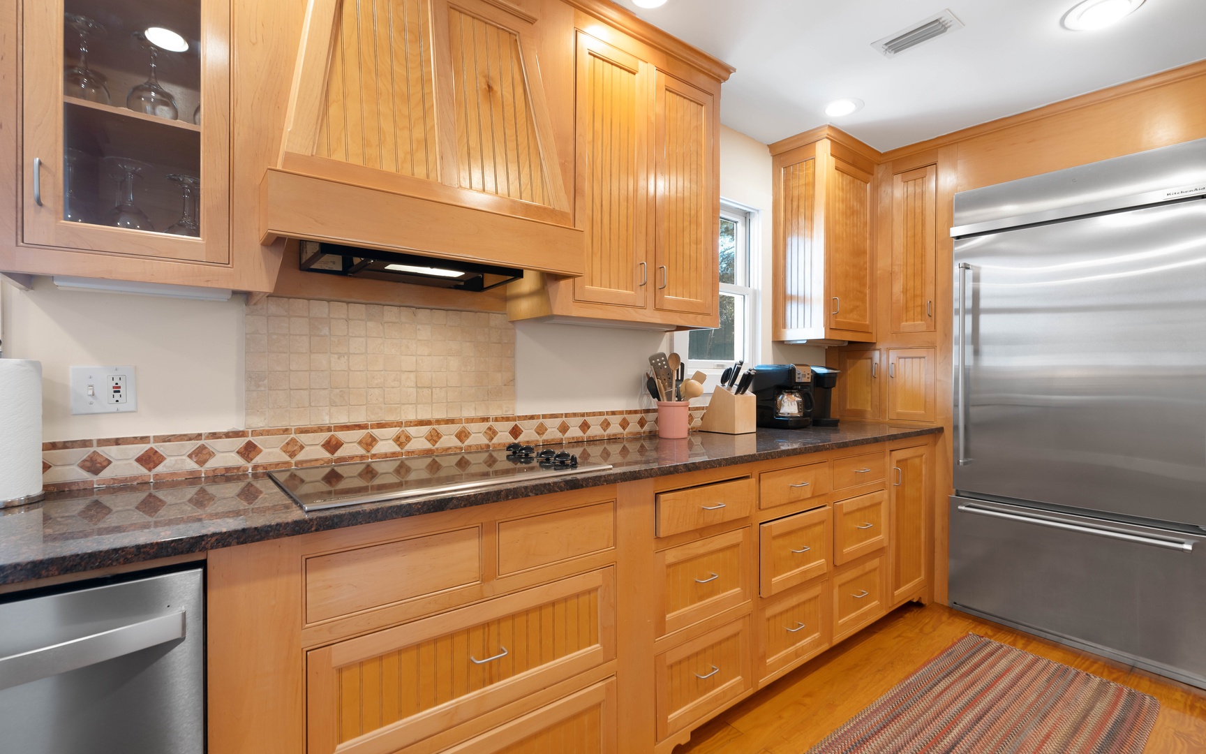 Prepare delicious meals in this elegant kitchen featuring warm wood cabinetry, granite countertops, and modern appliances for your culinary adventures.