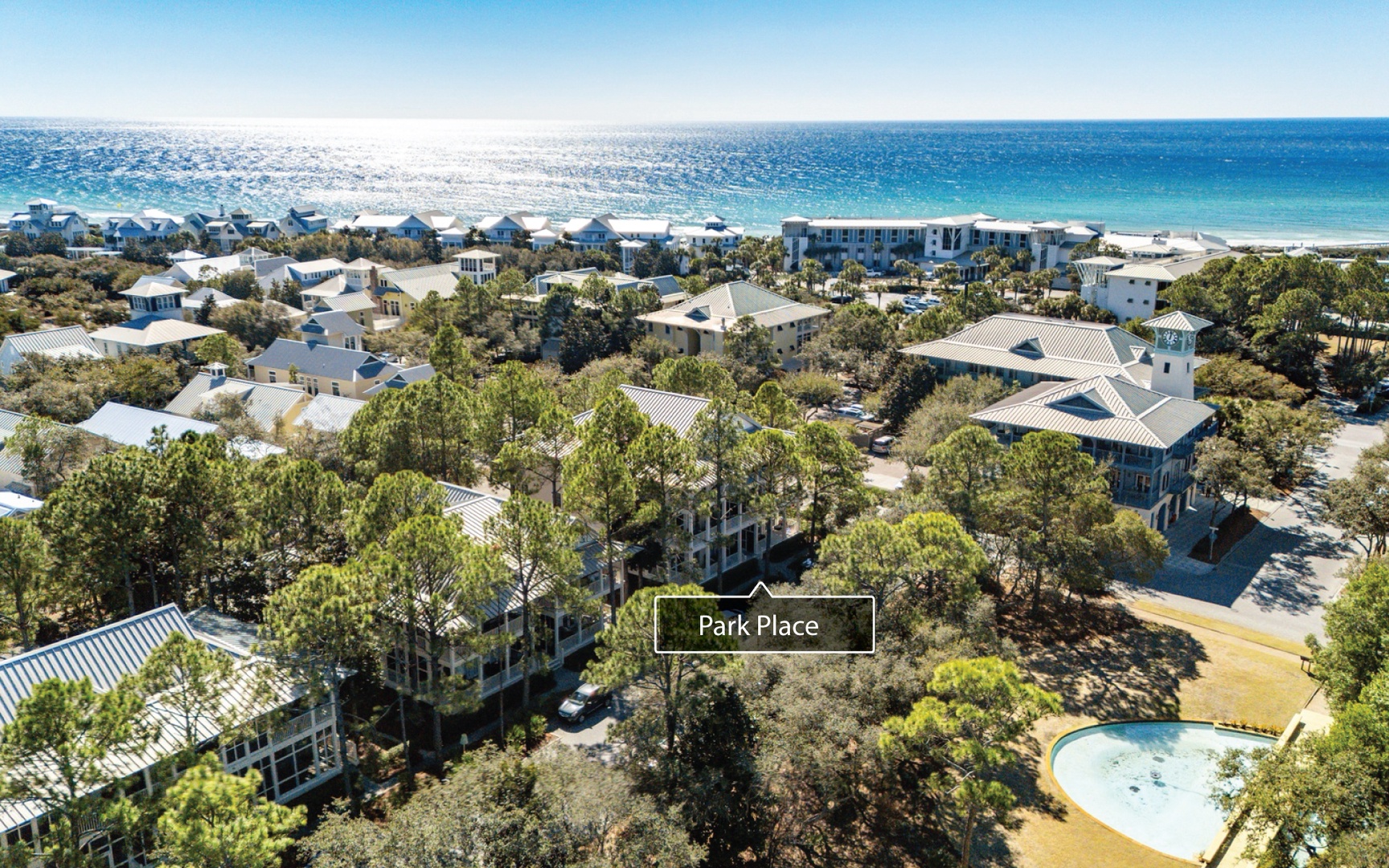 Aerial view of coastal vacation homes nestled among lush trees with crystal blue waters and pristine beach nearby.