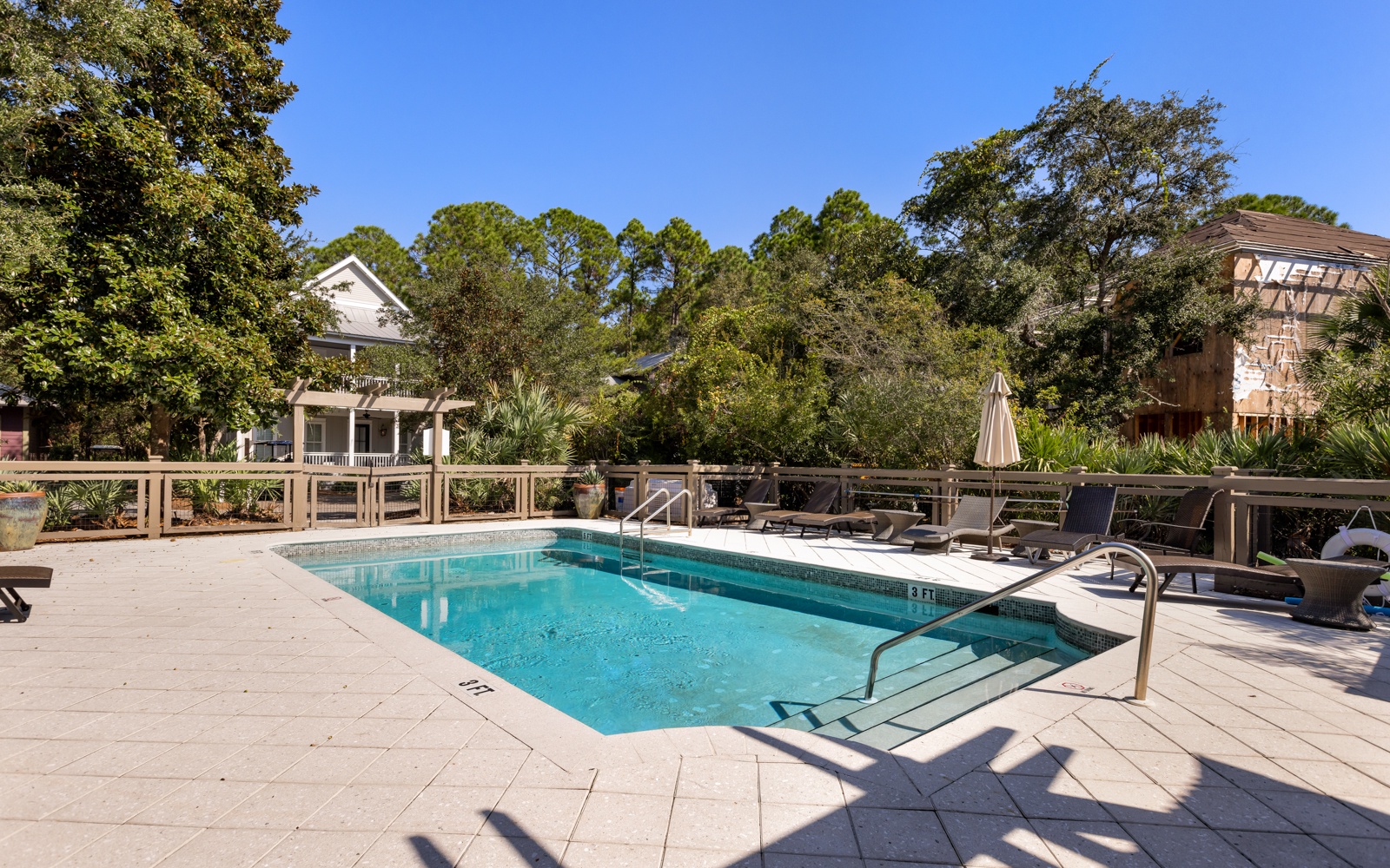 Dive into crystal-clear waters surrounded by mature trees and comfortable lounge chairs for your perfect poolside retreat.