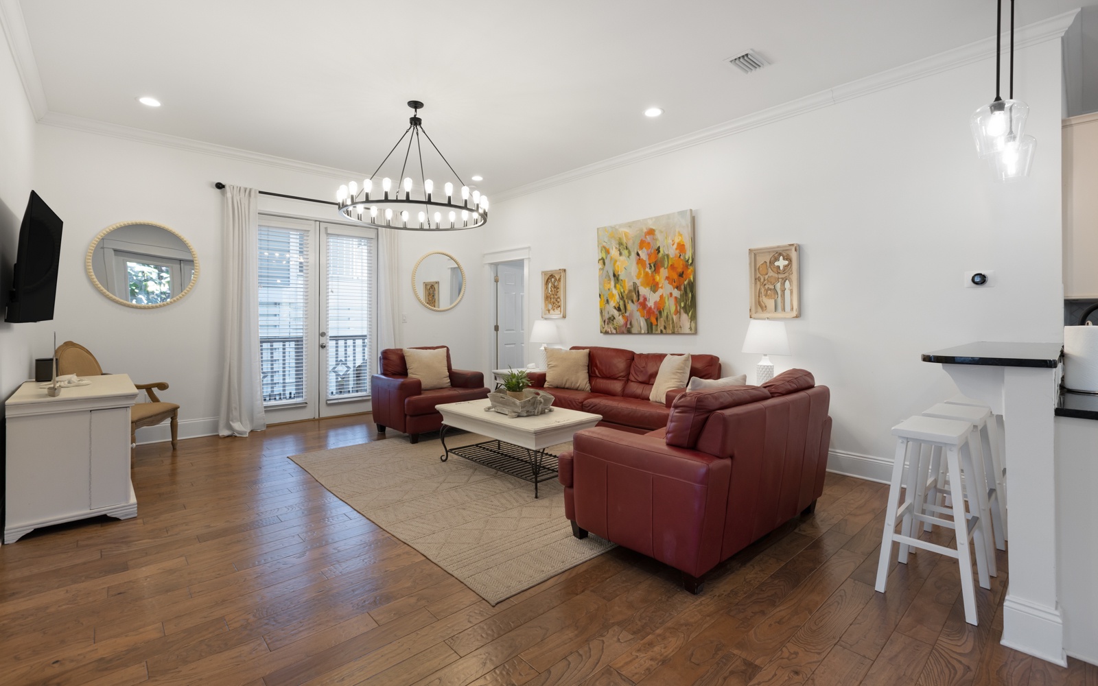 Gather with friends in your stylish living room featuring rich burgundy leather seating, warm hardwood floors, and elegant lighting.
