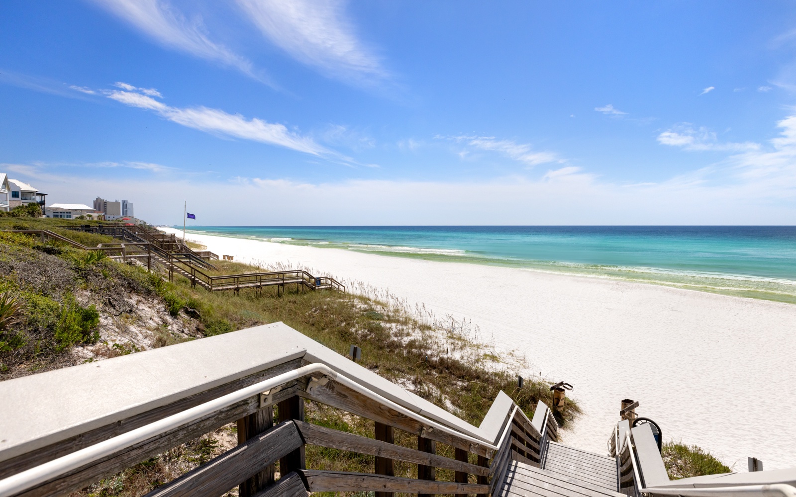 Pristine white sand beach stretches along crystal-clear turquoise waters under brilliant blue skies, with convenient wooden boardwalk access.