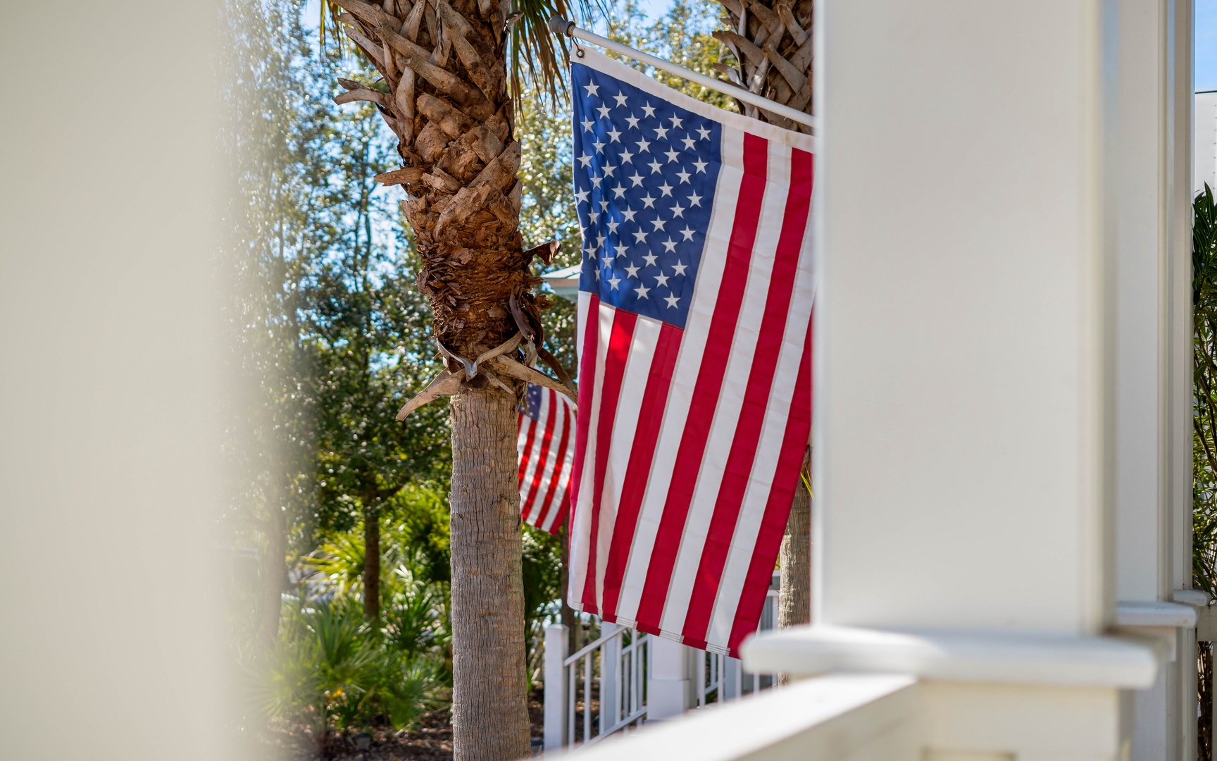 American flag proudly displays at the property entrance, welcoming guests with patriotic charm amid lush palm trees and tropical landscaping.