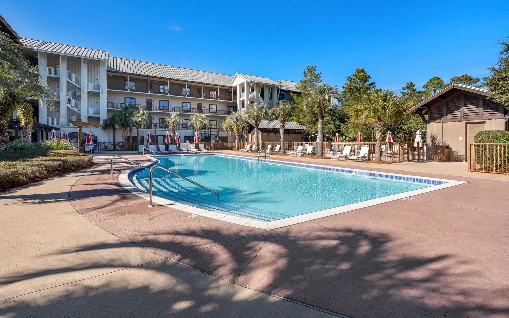 Resort-style pool surrounded by palm trees and comfortable lounge chairs beneath bright blue skies.