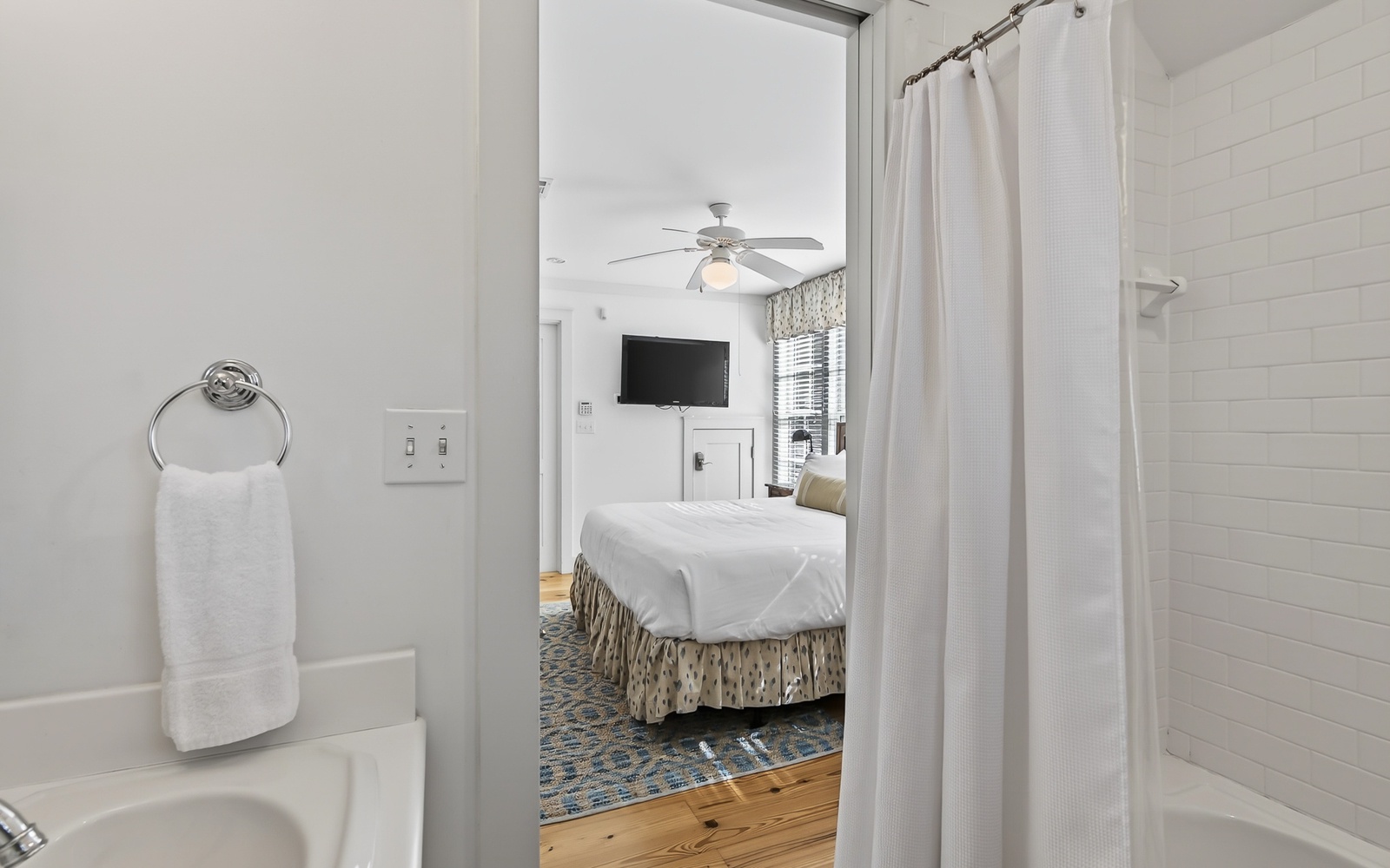 Step from your pristine white bathroom into your cozy bedroom, where crisp linens and warm wood floors create the perfect retreat.