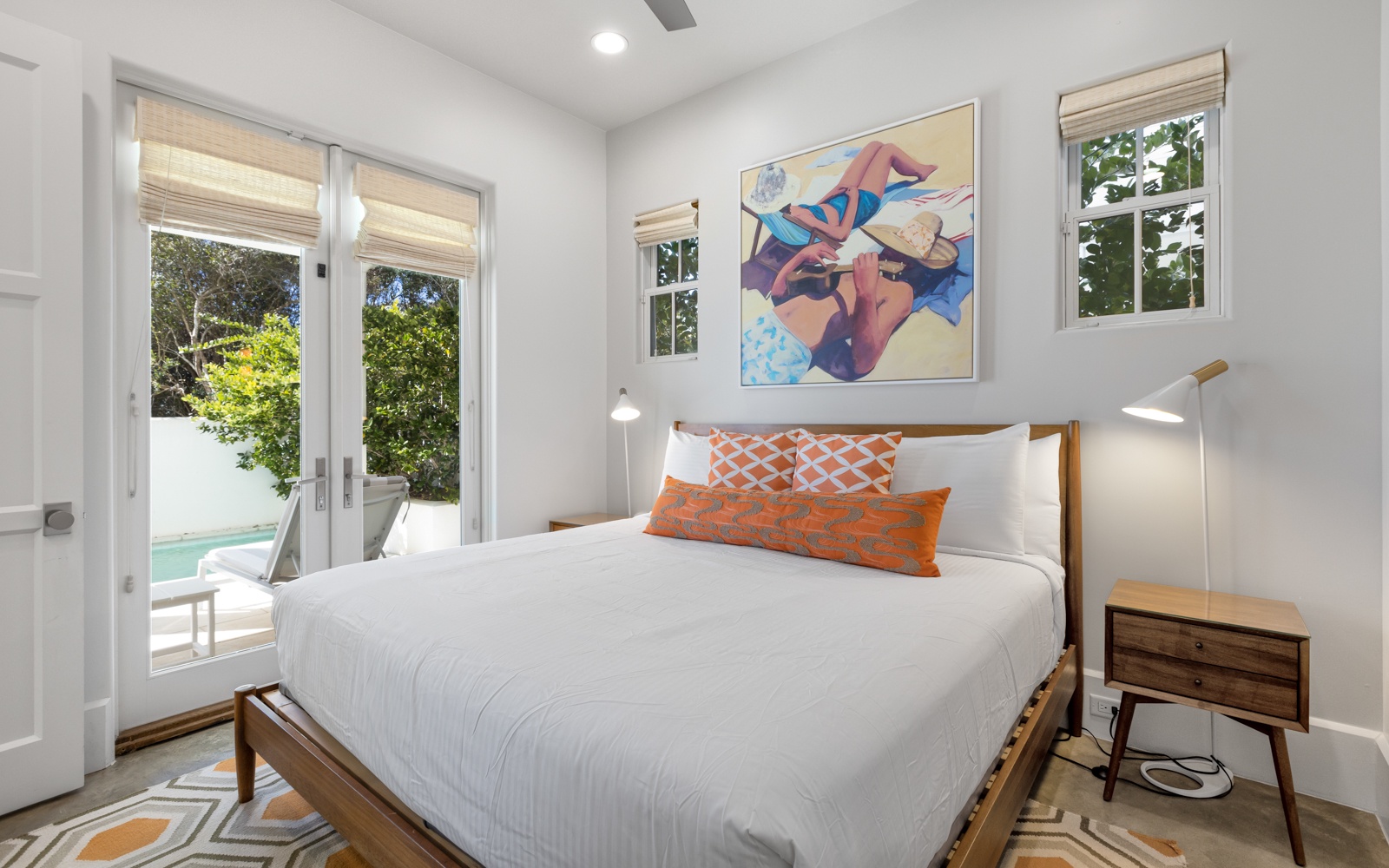Your bright bedroom opens to poolside paradise through French doors, featuring crisp linens and modern artwork for peaceful nights.