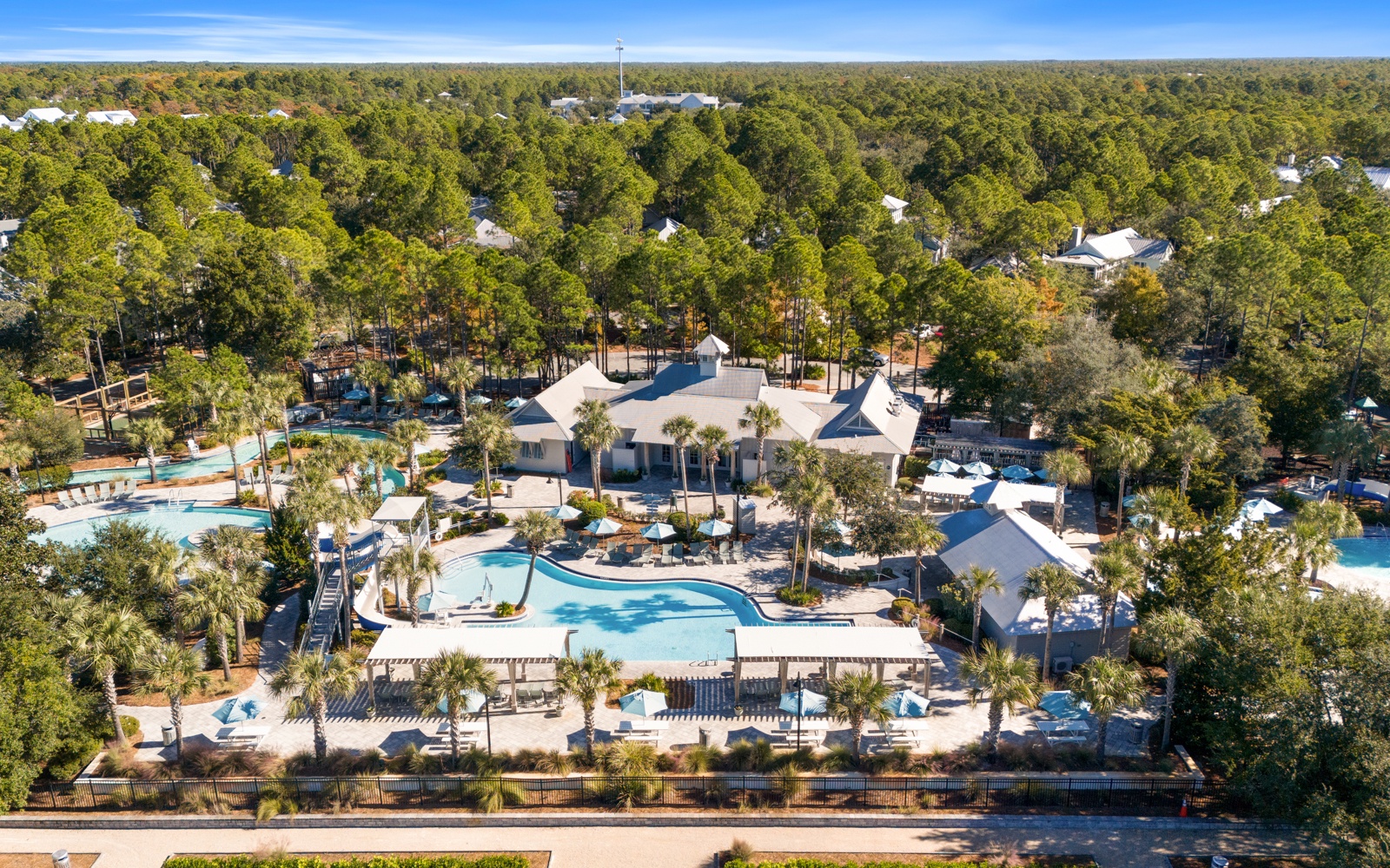 Aerial view of resort-style community featuring multiple pools, clubhouse, and lush landscaping nestled among mature trees.