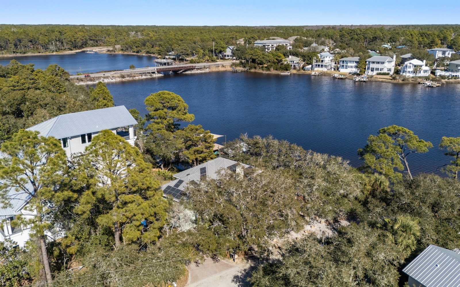 Aerial view of waterfront properties nestled among mature trees along a pristine lake with neighboring vacation homes visible across the water.