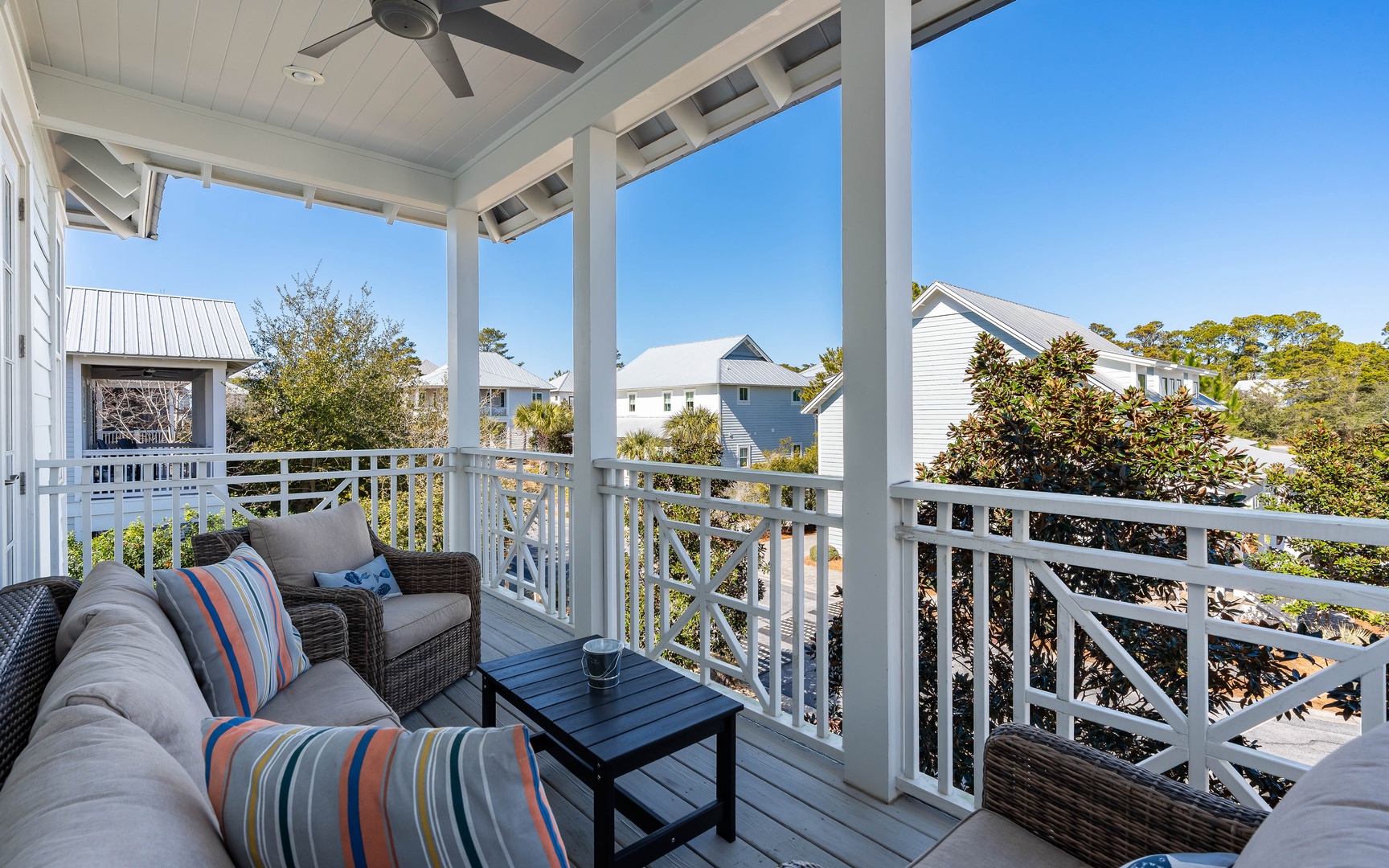 Relax on your private covered balcony with comfortable seating, enjoying peaceful neighborhood views under clear blue skies.
