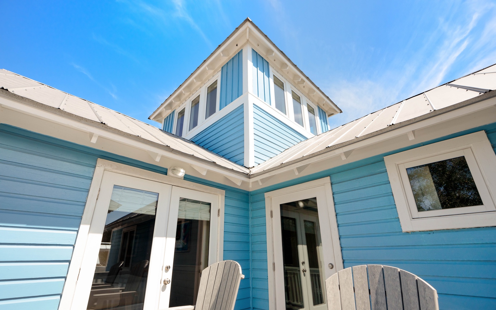 Charming coastal-style home with turquoise siding and white trim under brilliant blue skies.