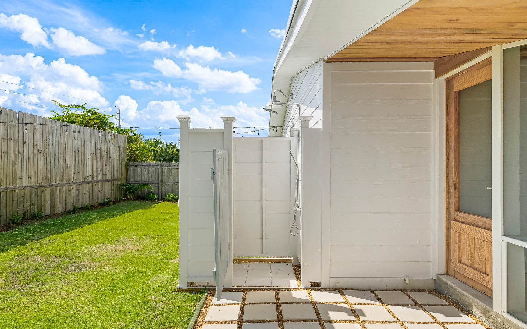 Modern outdoor shower with private walls and natural stone flooring, surrounded by lush green lawn and wooden fencing.