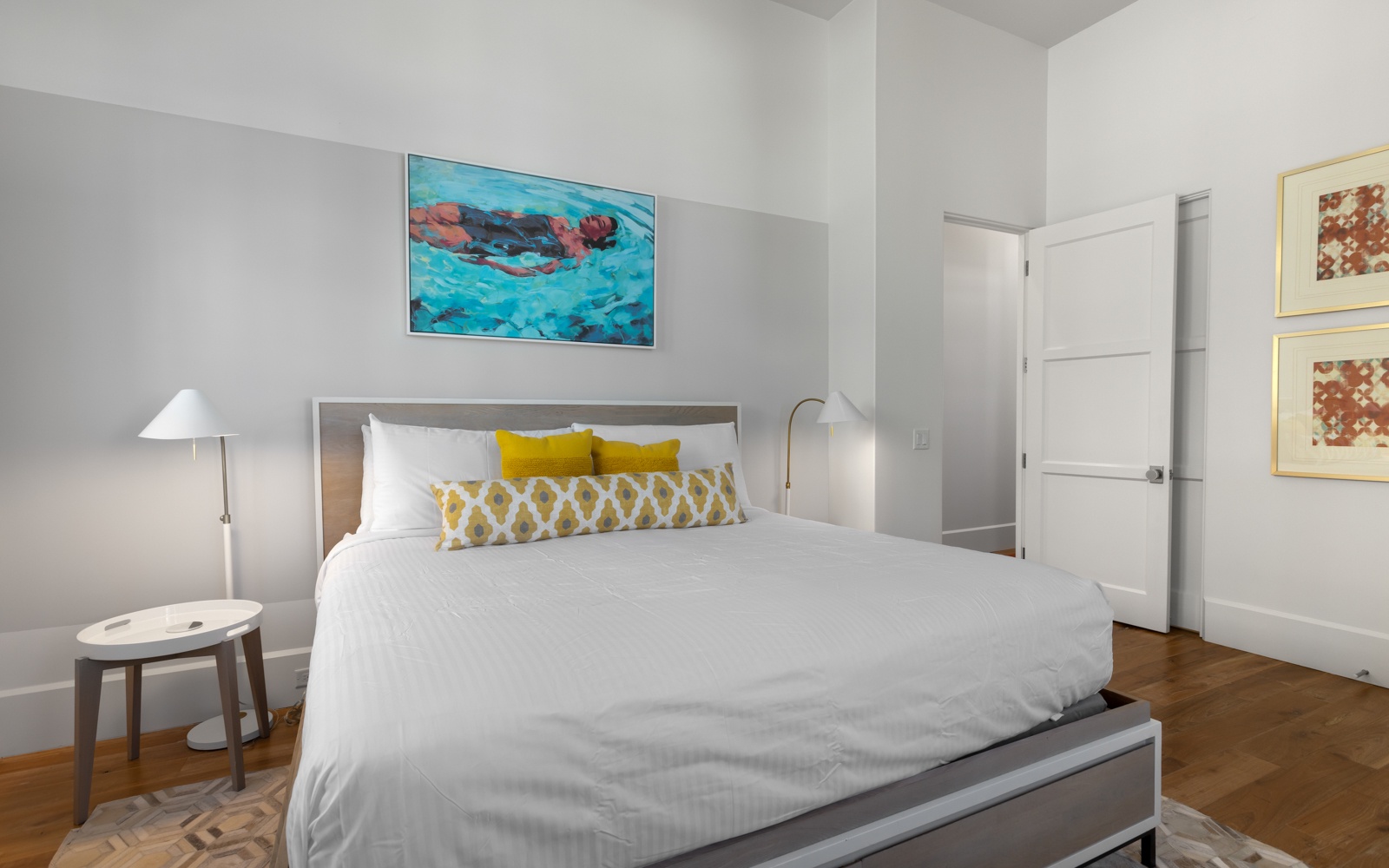 Sink into crisp white linens and vibrant yellow accents in your stylish bedroom sanctuary, where coastal artwork and warm lighting create the perfect retreat.