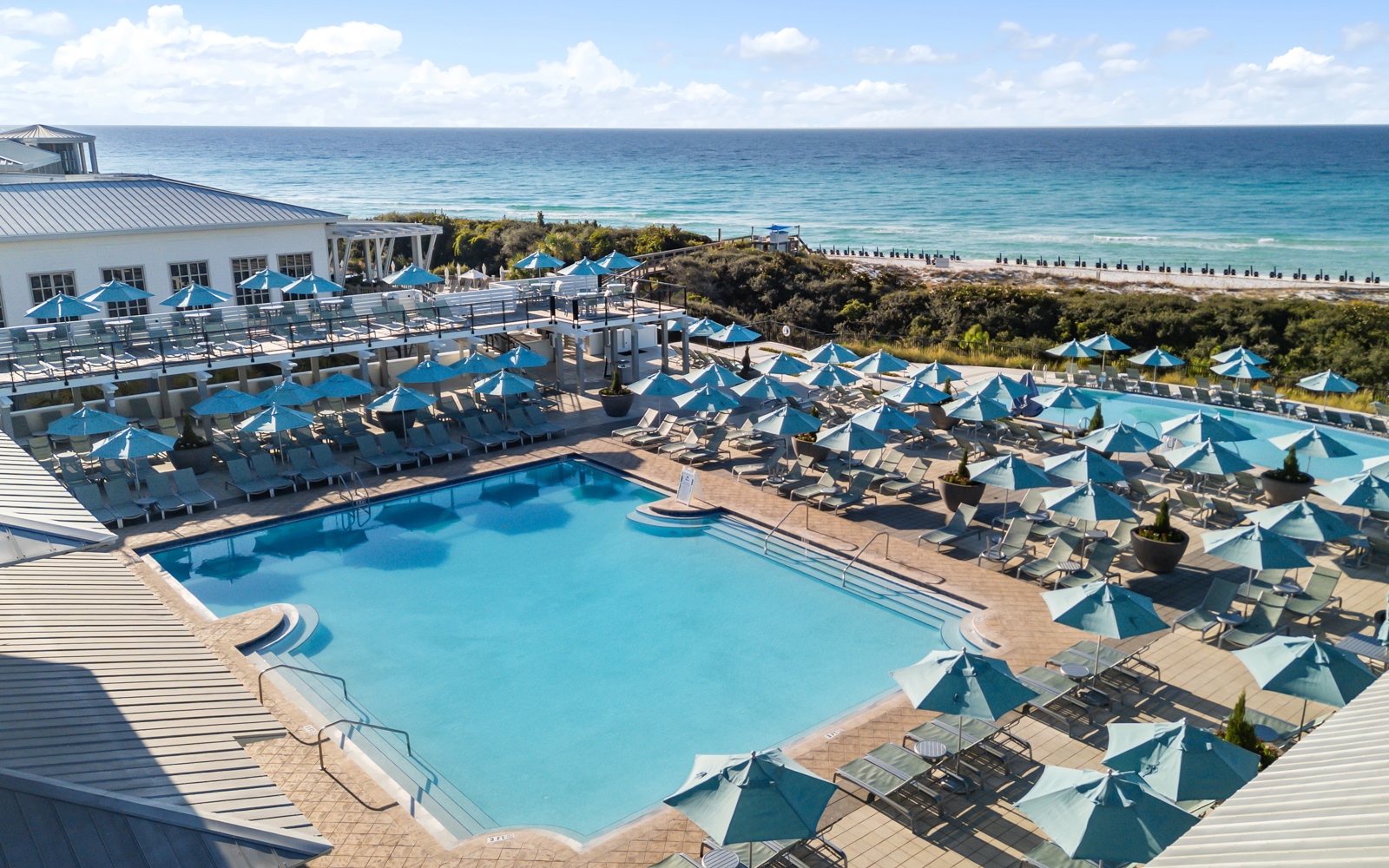 Beachfront resort featuring expansive pool area with turquoise umbrellas overlooking pristine white sand beach and crystal-clear ocean waters.