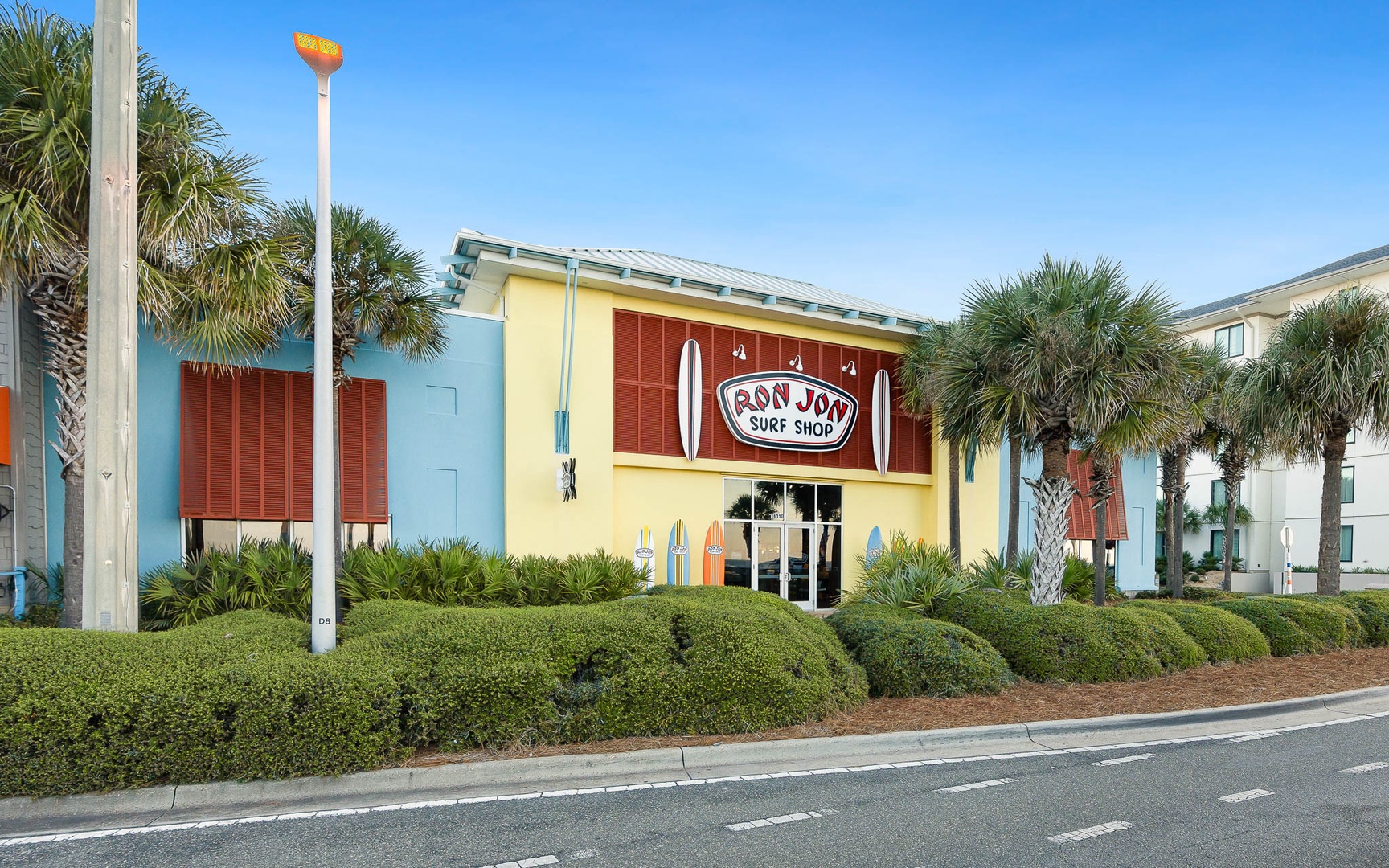 Ron Jon Surf Shop sits among colorful beach buildings with palm trees lining the street in this vibrant coastal neighborhood.