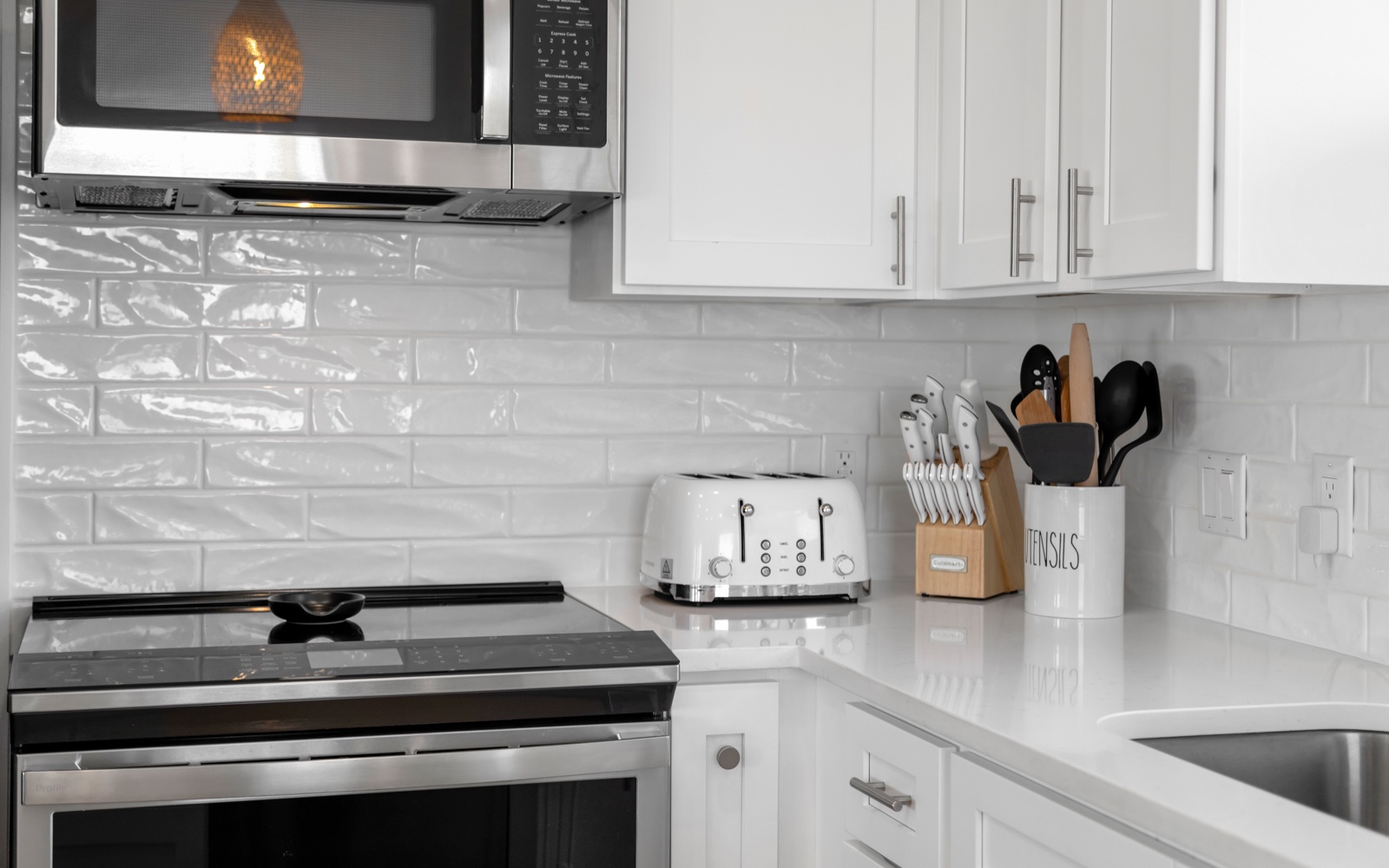 Your modern kitchen features sleek white cabinetry, quartz countertops, and all essential appliances including microwave, toaster, and stove for effortless meal preparation.