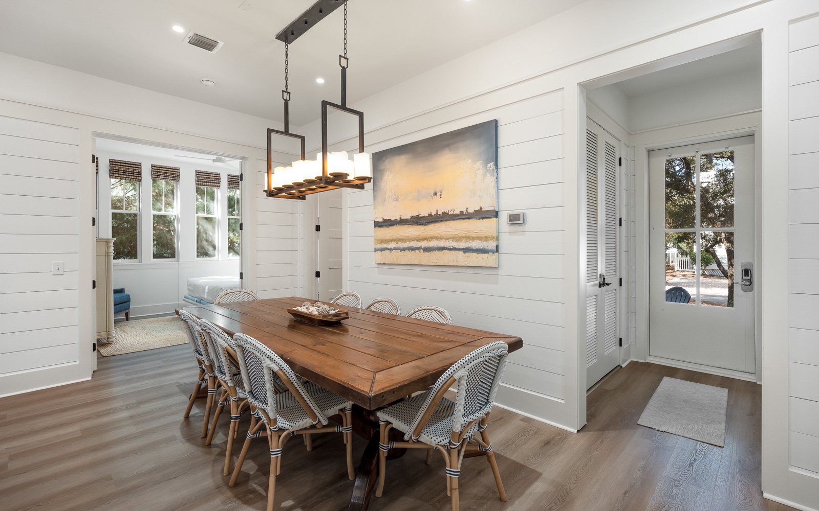Gather around this stunning dining table where coastal artwork and warm lighting create the perfect setting for your memorable meals together.