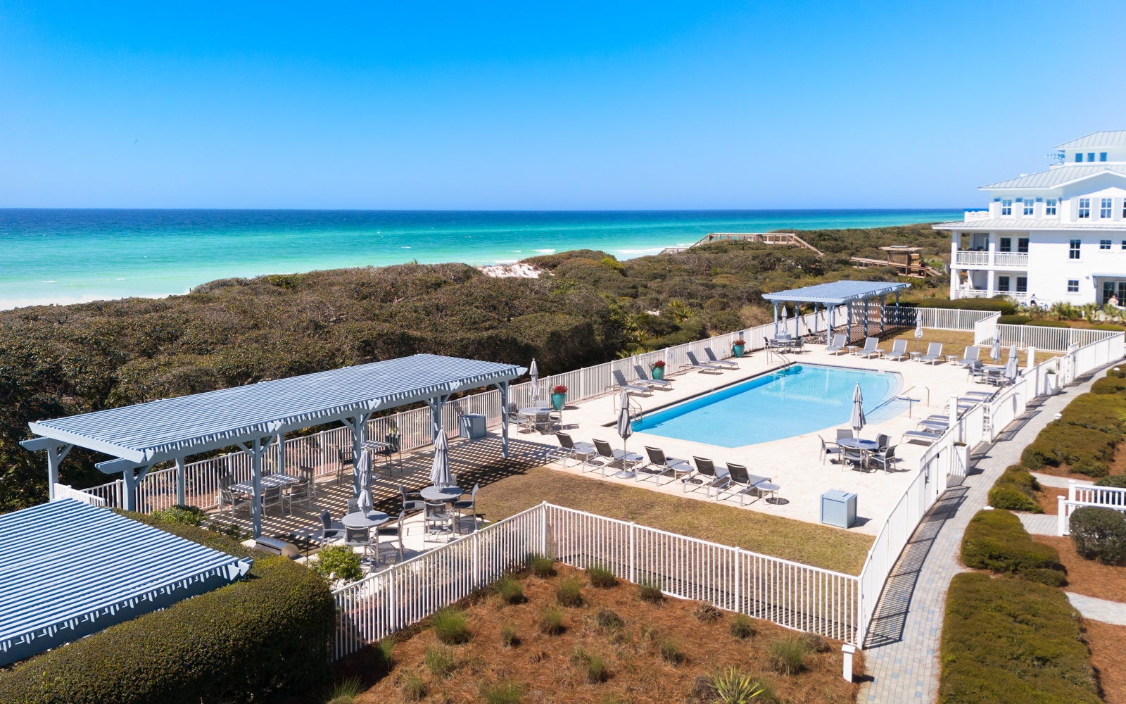 Beachfront property featuring elevated pool deck with pristine white sand beach and turquoise waters beyond natural dune vegetation.