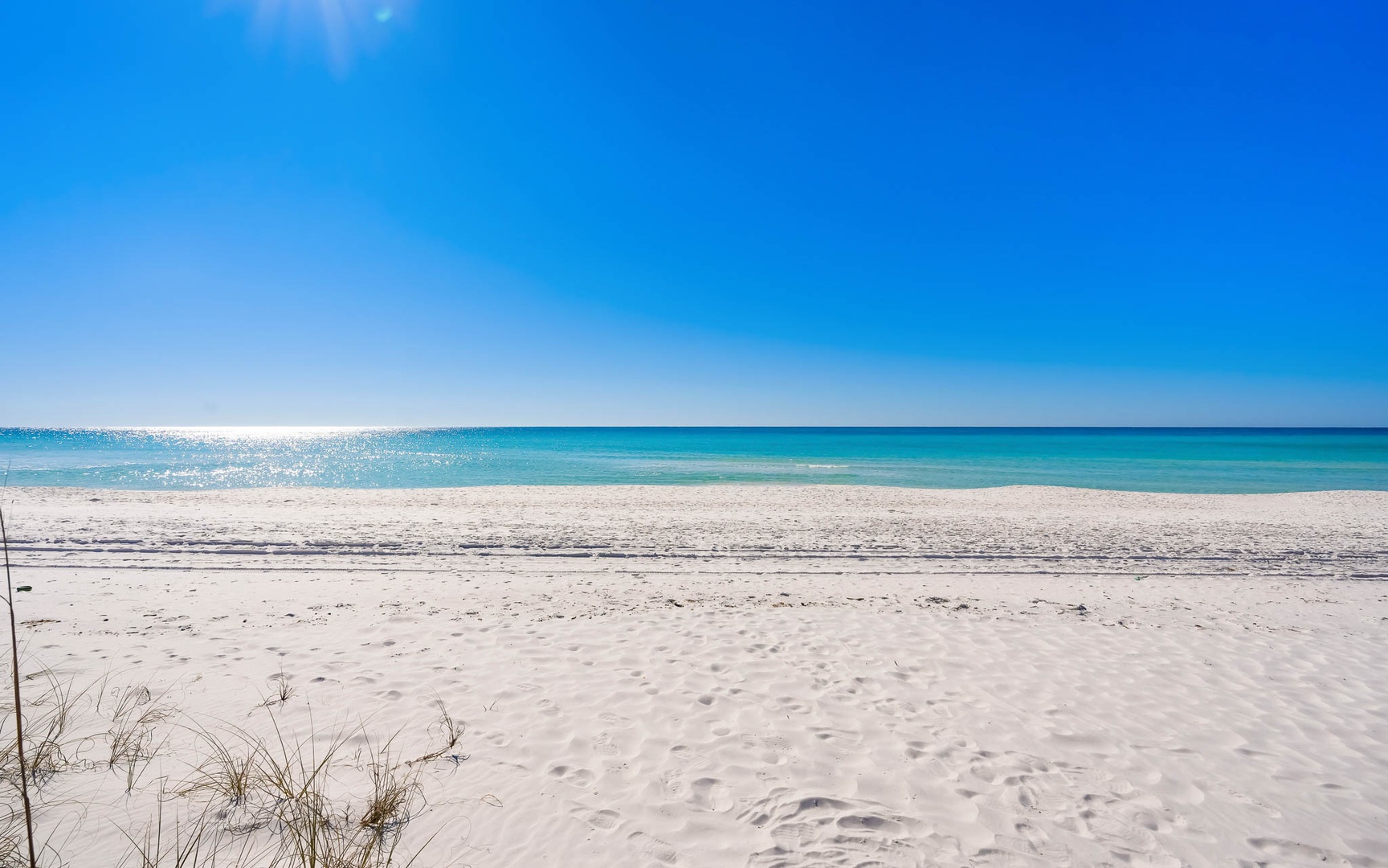 Pristine white sand beach stretches endlessly under brilliant blue skies, with crystal-clear turquoise waters perfect for swimming and relaxation.