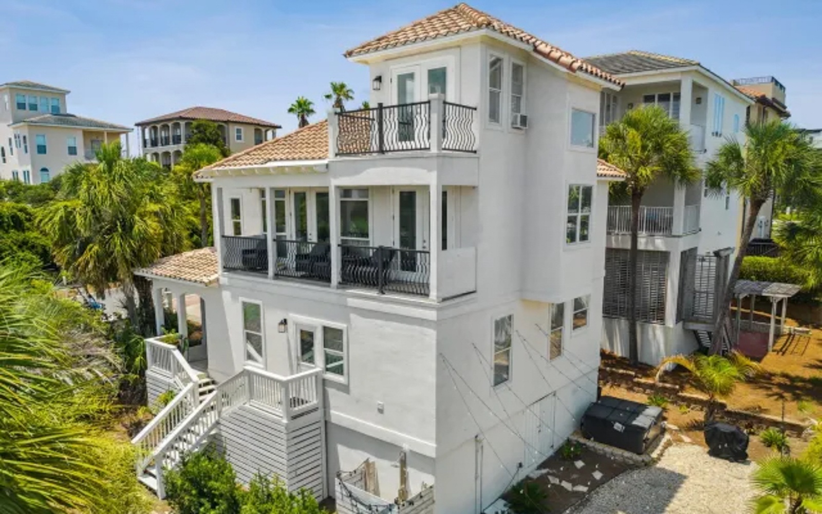 Modern three-story vacation home with Mediterranean tile roof and multiple balconies in a tropical coastal neighborhood.