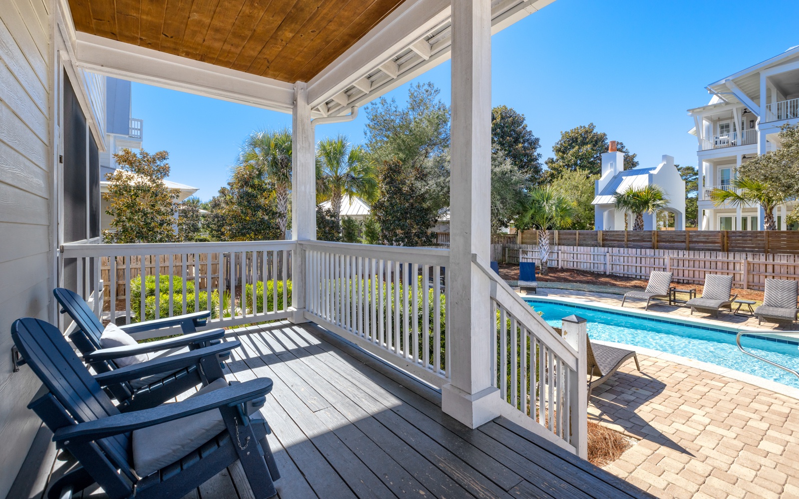 Your private covered porch overlooks the sparkling pool, perfect for morning coffee or evening relaxation with those comfy blue Adirondack chairs.