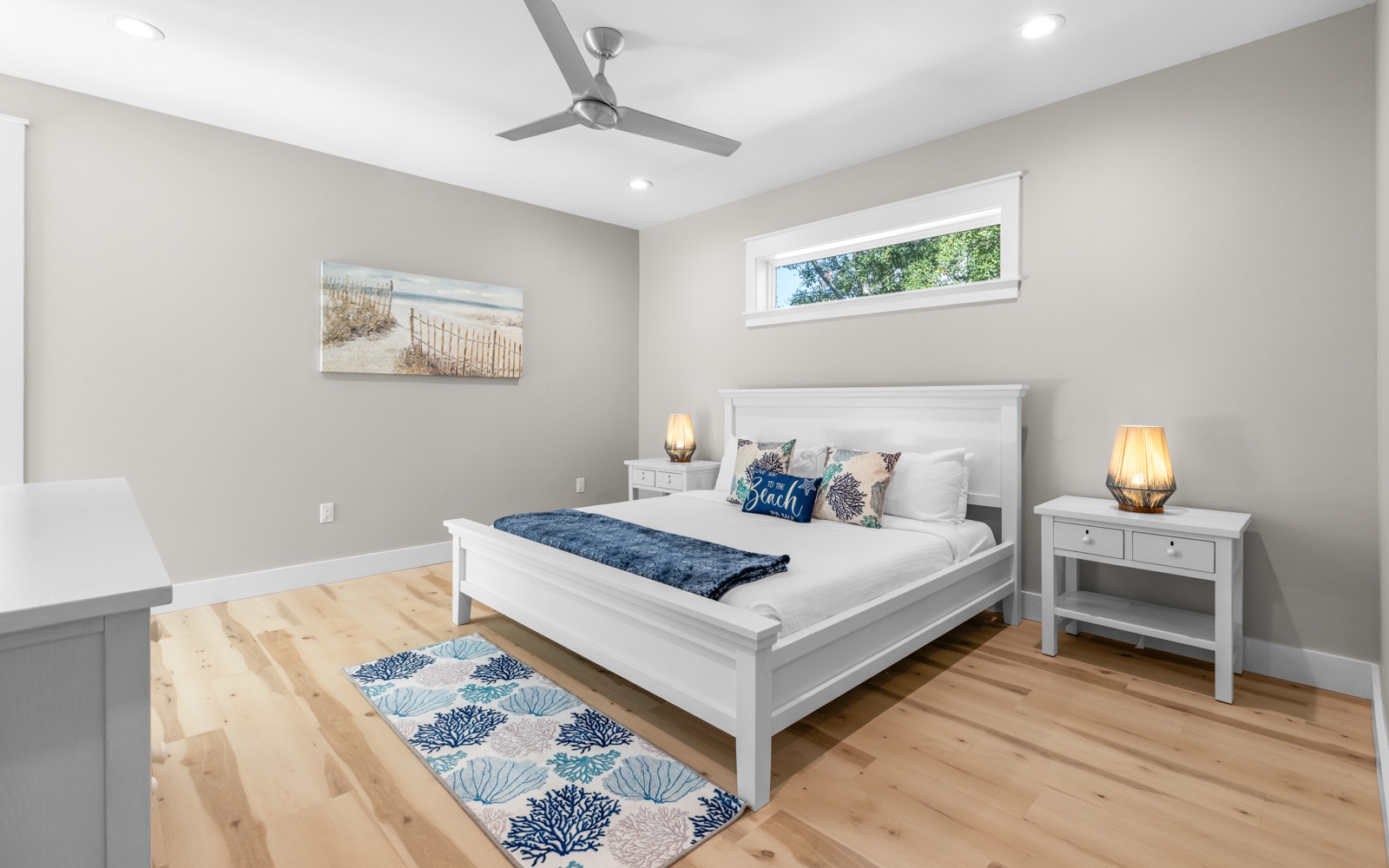 Drift off to peaceful sleep in your serene bedroom, featuring warm wood floors, coastal artwork, and gentle ceiling fan breezes.