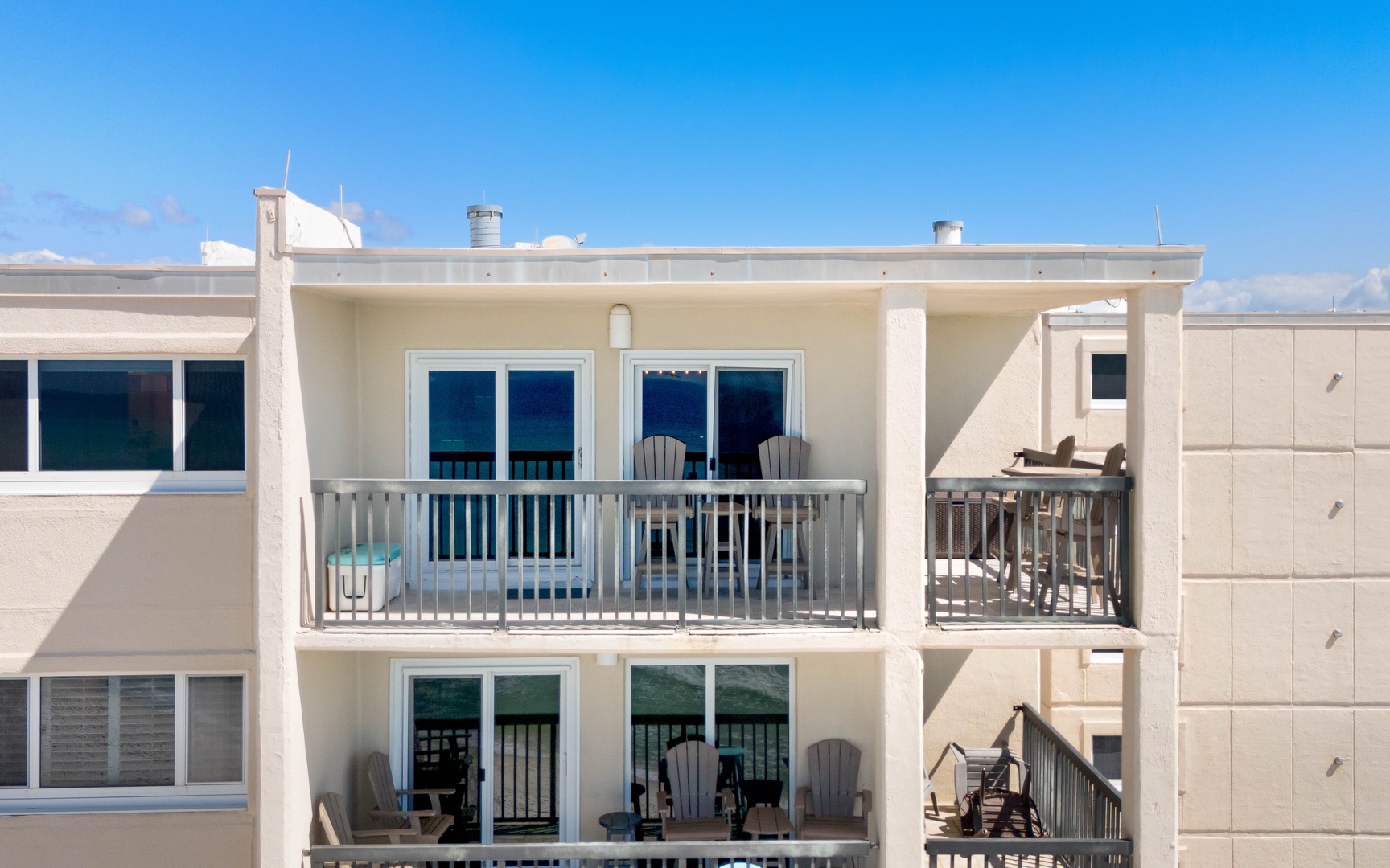 Modern beachside property featuring spacious balconies with ocean-facing views and comfortable outdoor seating under clear blue skies.