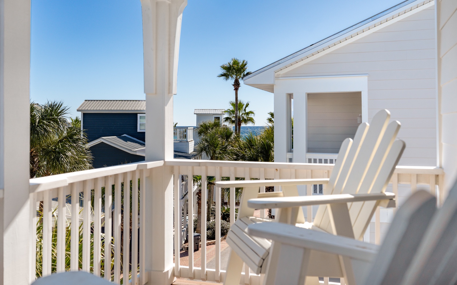 Coastal charm awaits on this bright balcony with comfortable seating and tropical views of neighboring homes and palm trees.