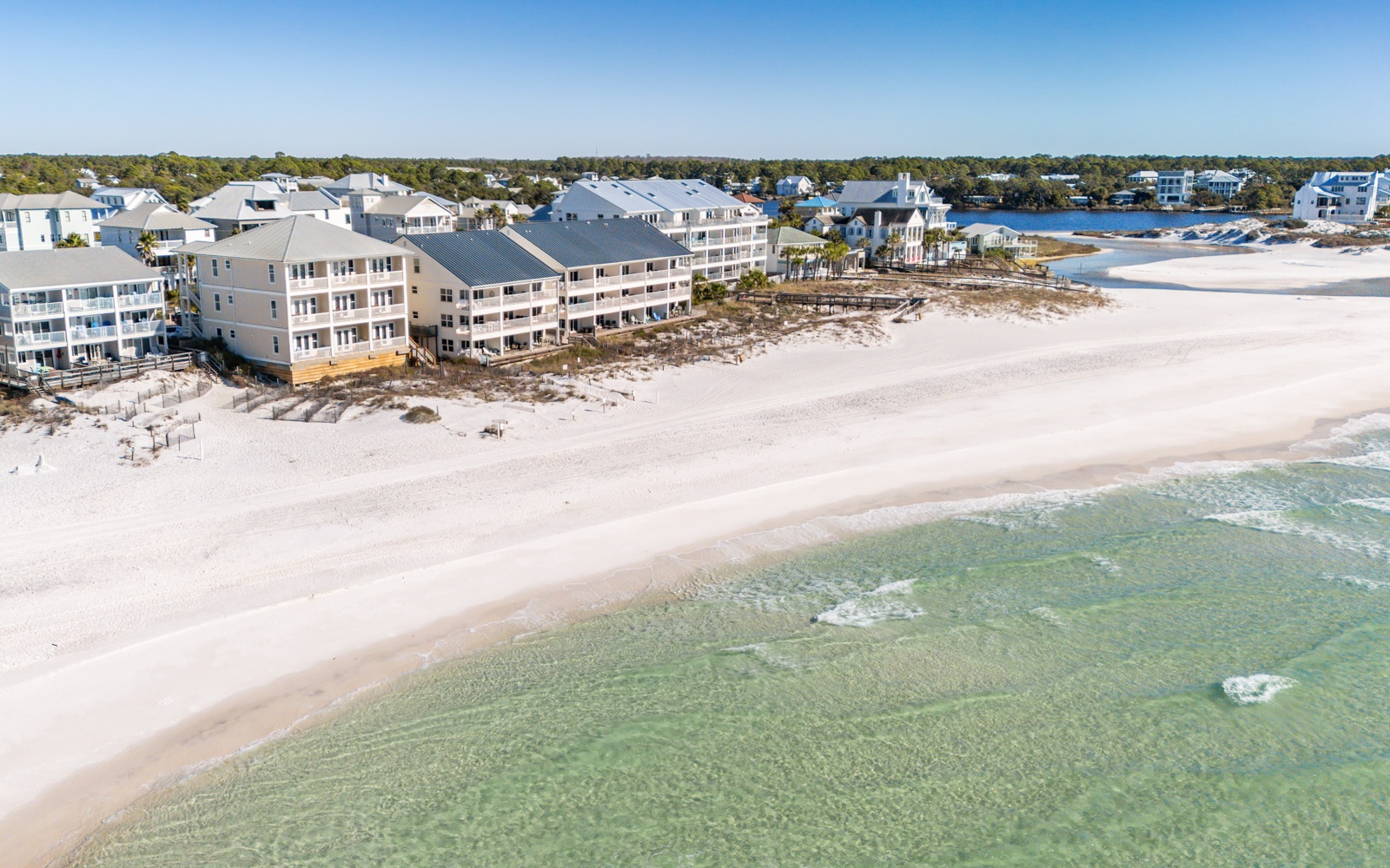 Aerial view of beachfront vacation rental properties situated directly on pristine white sand beach with crystal-clear emerald waters.