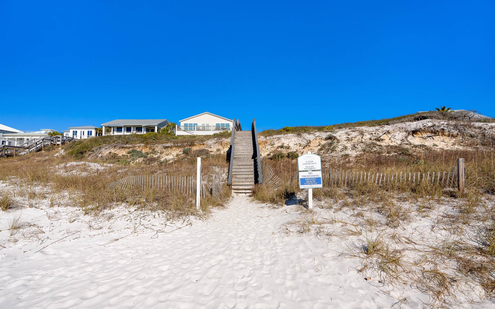 Beachfront vacation homes perched on sandy dunes with direct beach access via wooden boardwalk stairs.