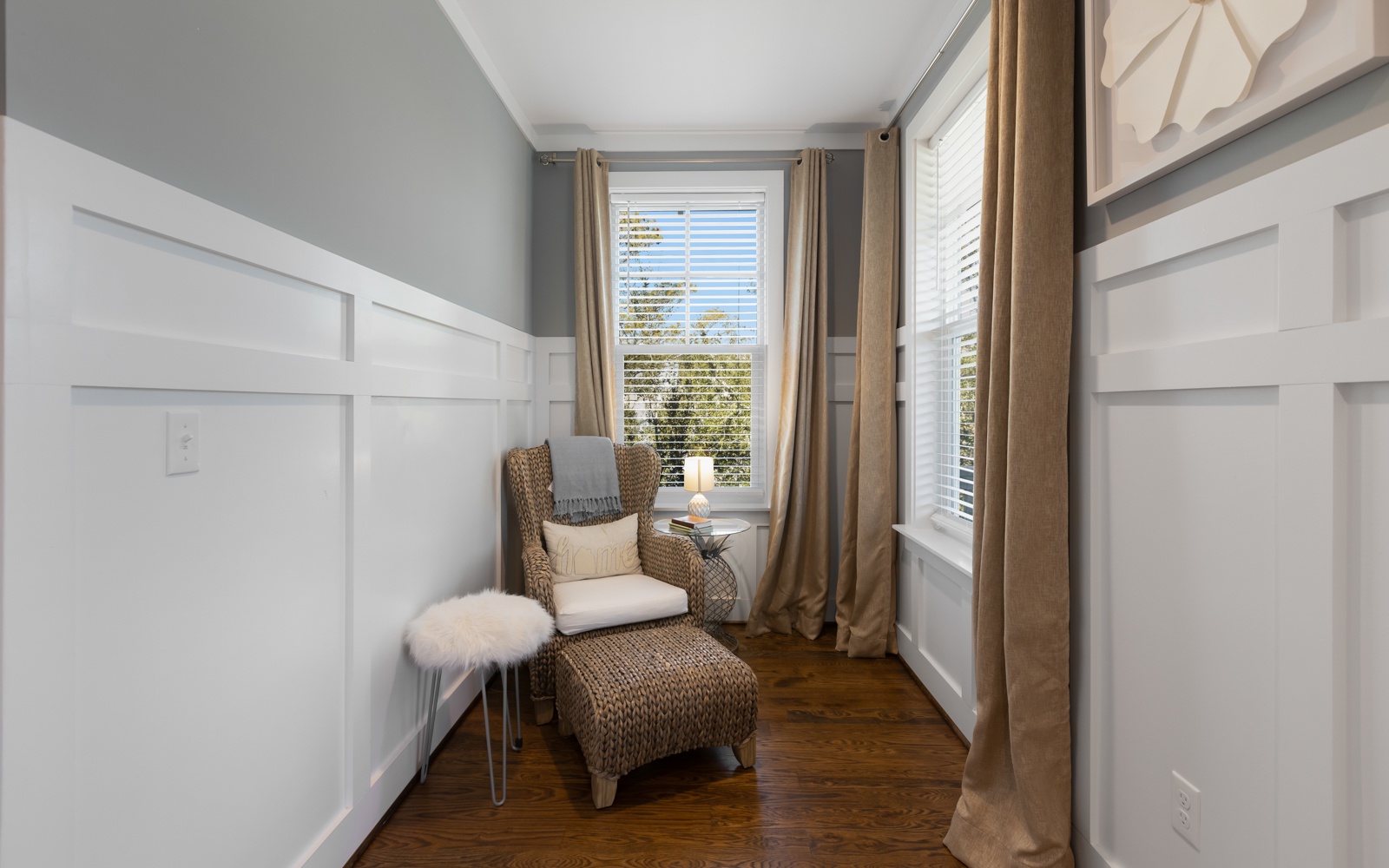 Cozy reading nook with wicker chair and ottoman where you can unwind with natural light streaming through plantation shutters.