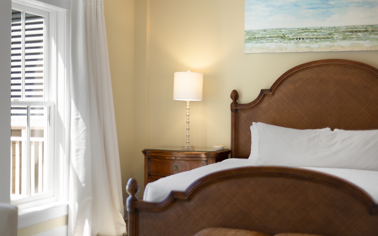 Sink into crisp white linens on your elegant bed, where warm lighting and coastal artwork create your perfect retreat.