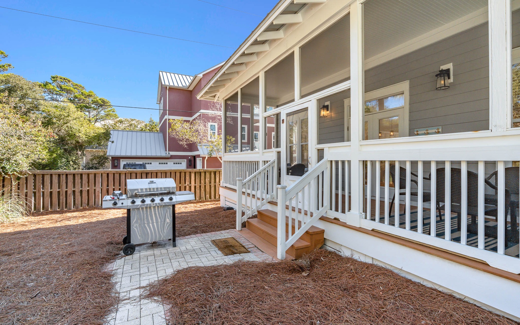 Modern vacation home exterior features covered porch with white railings and private fenced yard with grill for outdoor entertaining.
