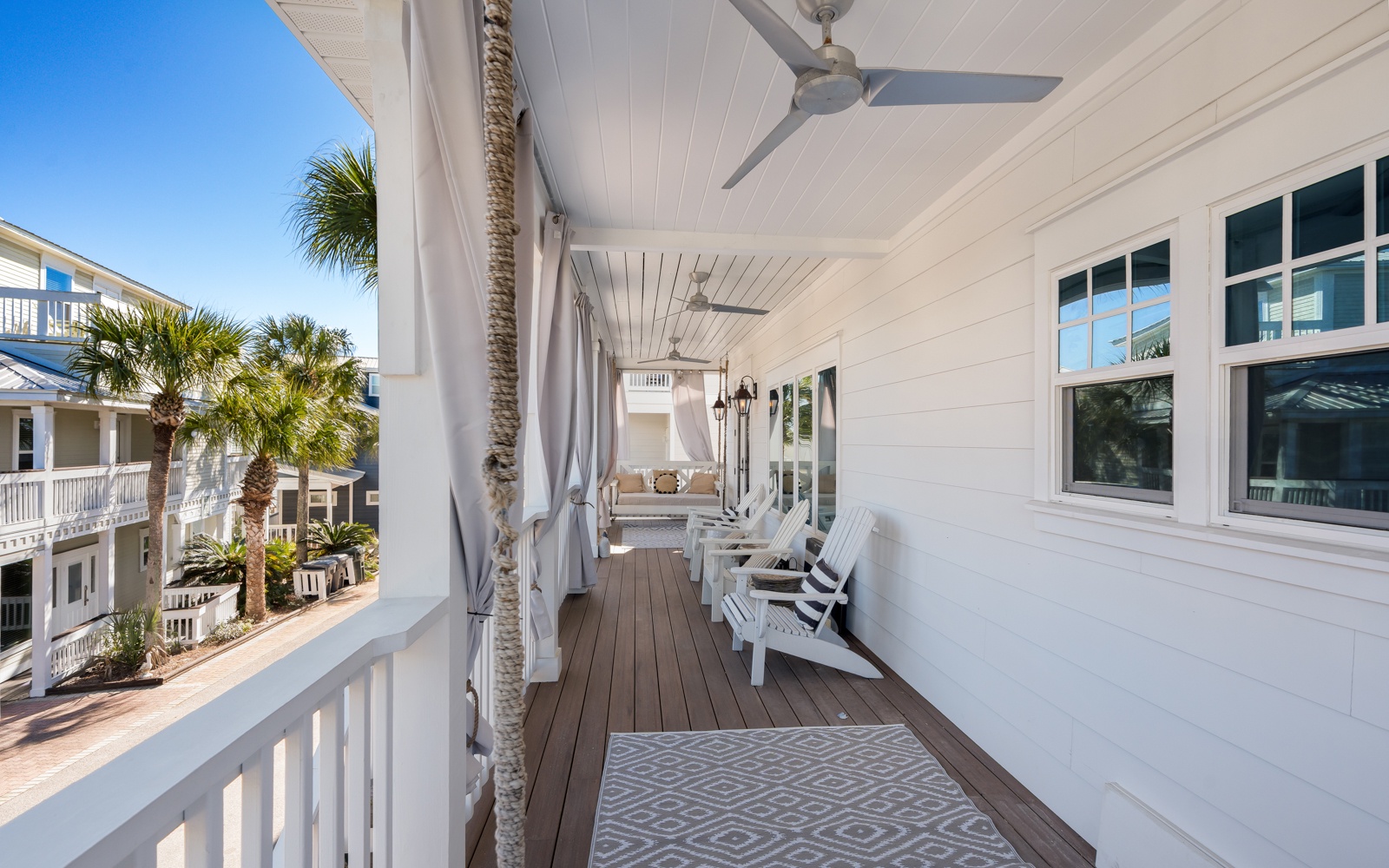 Your private covered porch invites relaxation with comfortable seating, ceiling fans, and peaceful views of palm trees and coastal architecture.