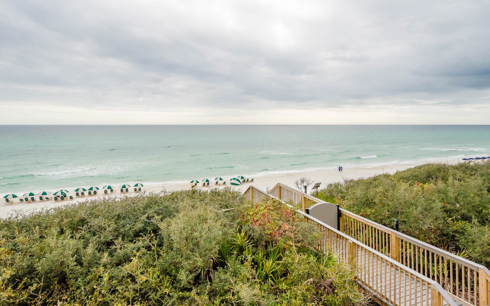 Elevated boardwalk leads to pristine beachfront with turquoise waters and rows of beach umbrellas creating a perfect coastal escape.