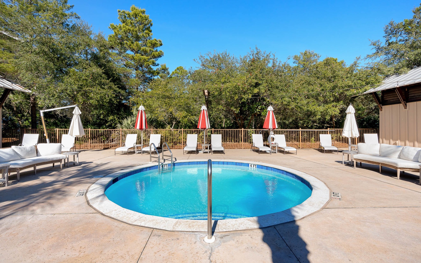 Sparkling outdoor pool surrounded by comfortable loungers and umbrellas, nestled in peaceful wooded surroundings for your perfect relaxation retreat.