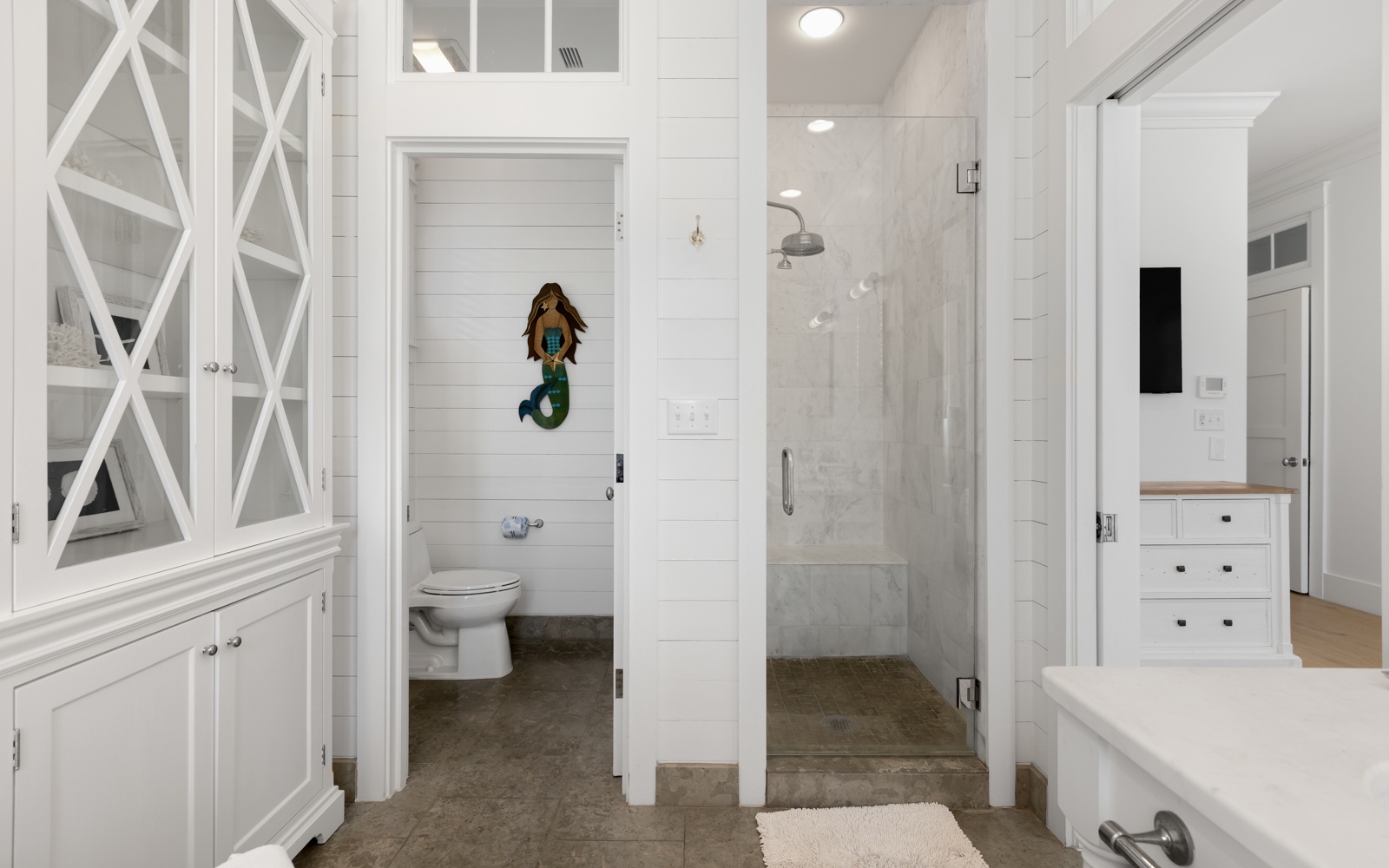 Step into your pristine spa-like bathroom featuring elegant marble shower, separate toilet, and crisp white cabinetry for a truly refreshing experience.