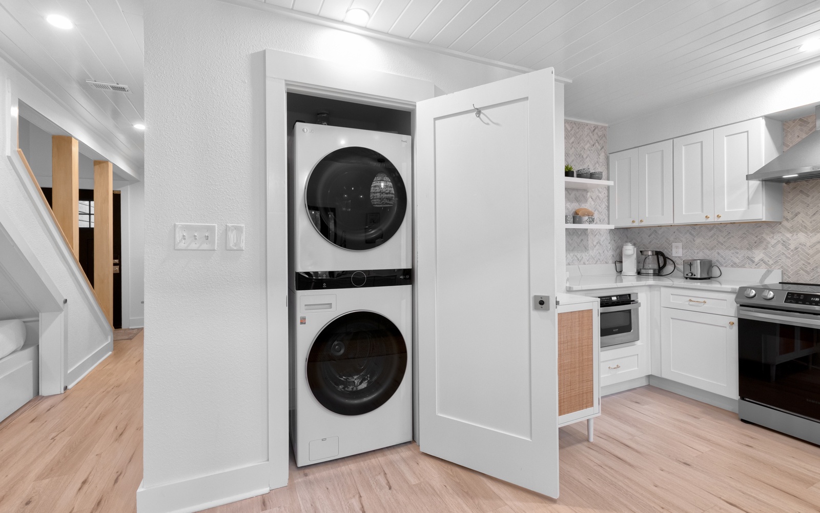 Your modern kitchen features a convenient built-in laundry closet with stackable washer and dryer, plus sleek white cabinets and contemporary appliances.
