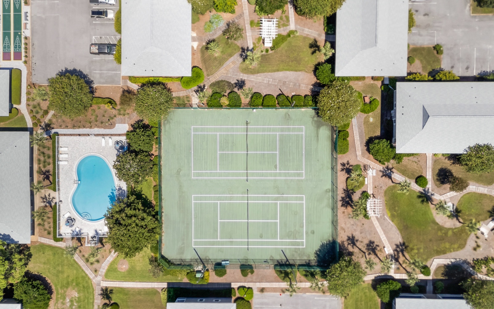 Aerial view shows property complex with tennis courts, swimming pool, and landscaped grounds surrounded by residential neighborhood.