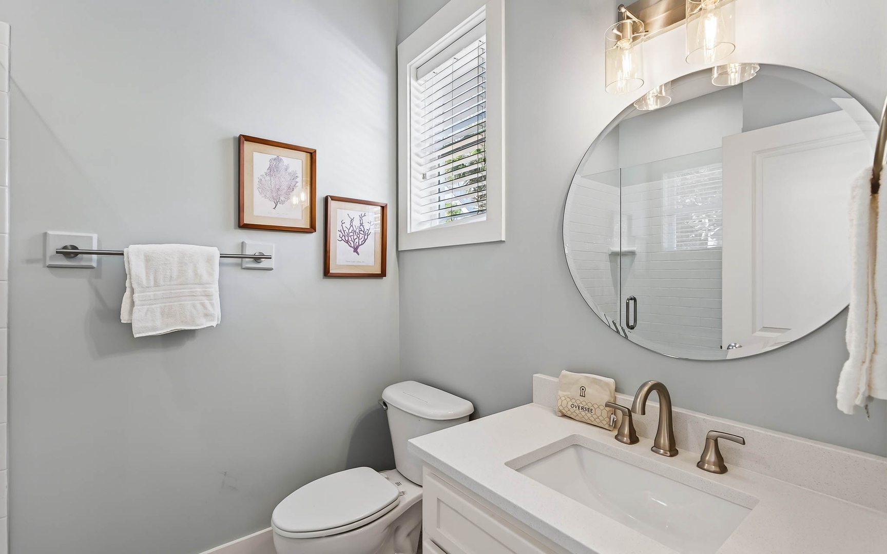Step into your elegant powder room featuring a quartz vanity, stylish round mirror, and coastal-inspired artwork that creates a spa-like atmosphere.