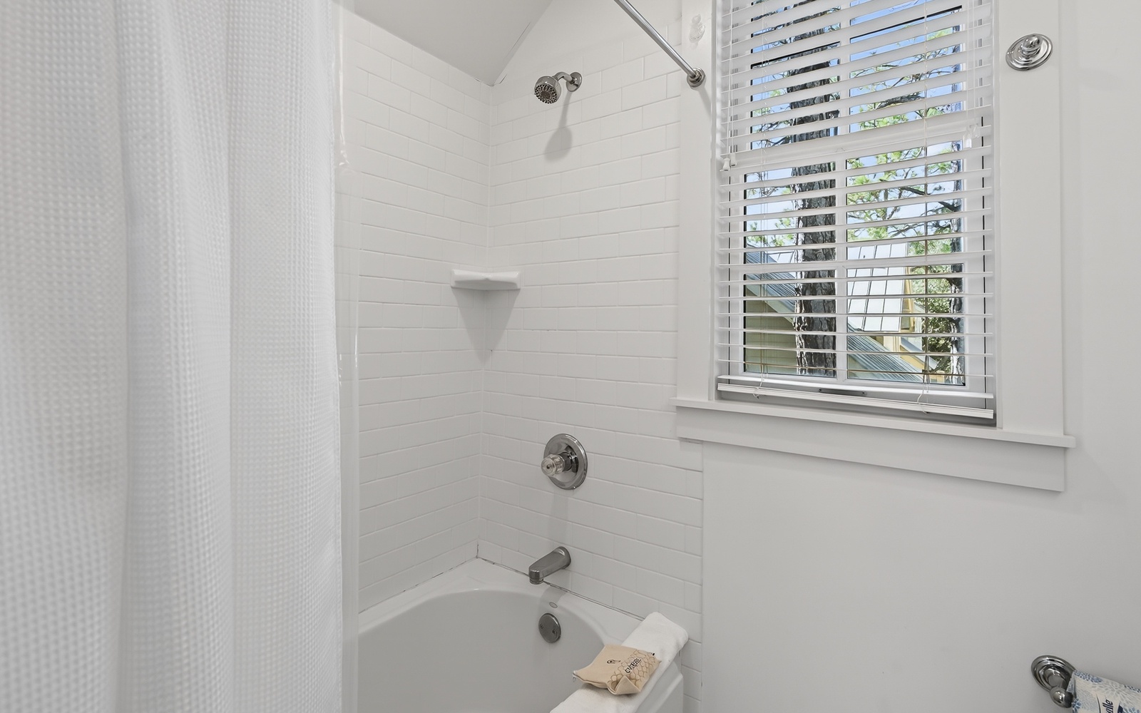 Step into your bright, modern bathroom featuring a spacious tub-shower combo with crisp white subway tiles and natural light streaming through plantation shutters.