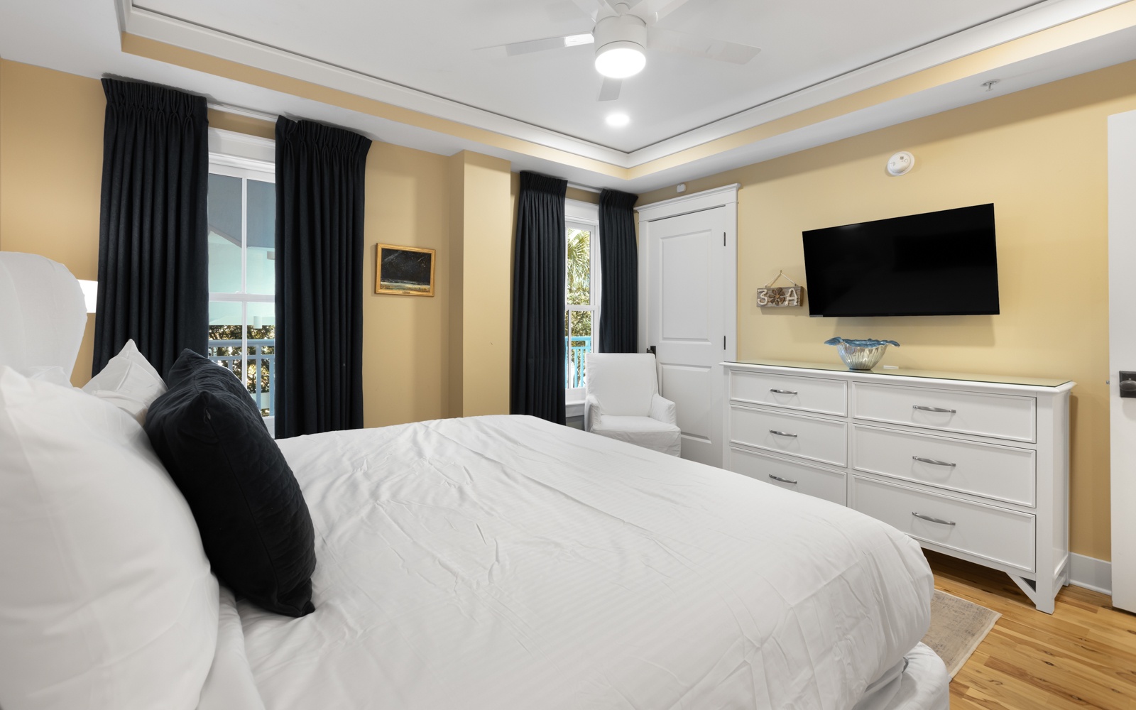 Sink into crisp white linens in your elegant bedroom, where warm golden walls and blackout curtains create a peaceful retreat.