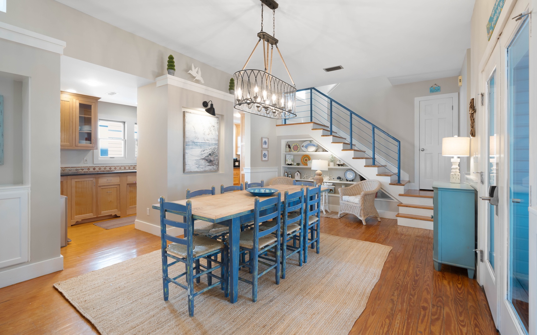 Coastal charm meets modern comfort in your open-plan living space, where blue accents and warm wood floors create the perfect backdrop for memorable meals.