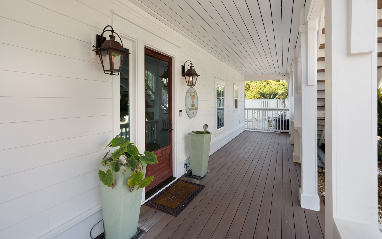 Step onto your private covered porch where charming lanterns and fresh greenery create a welcoming entrance to your coastal retreat.