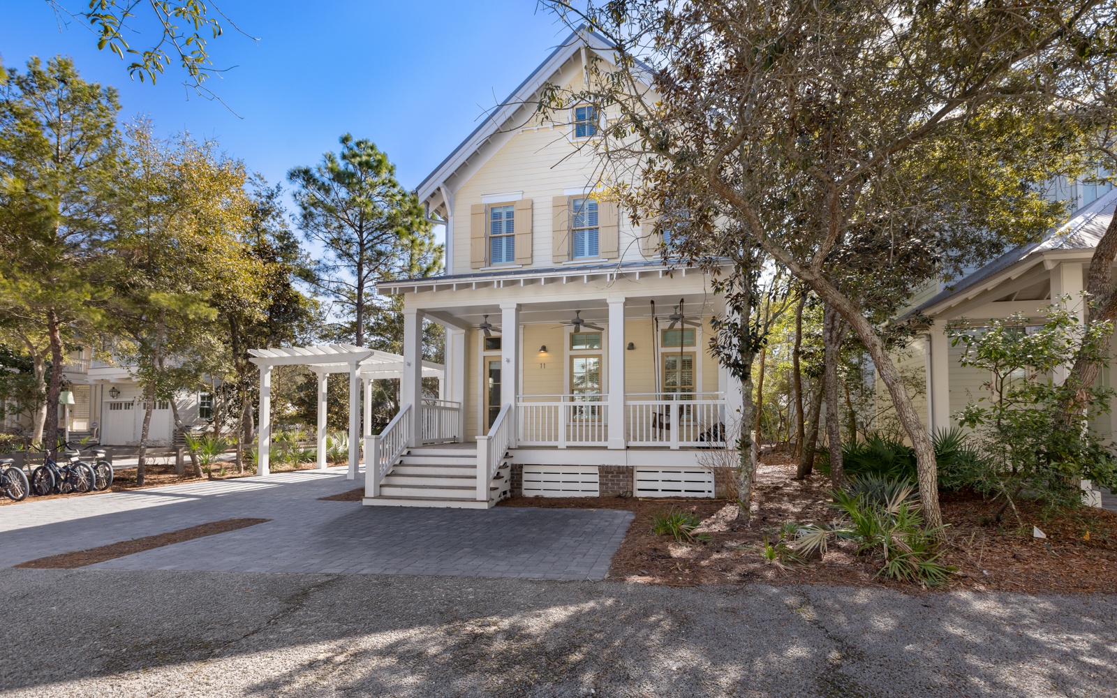 Charming coastal cottage with inviting front porch surrounded by mature trees and peaceful neighborhood setting.