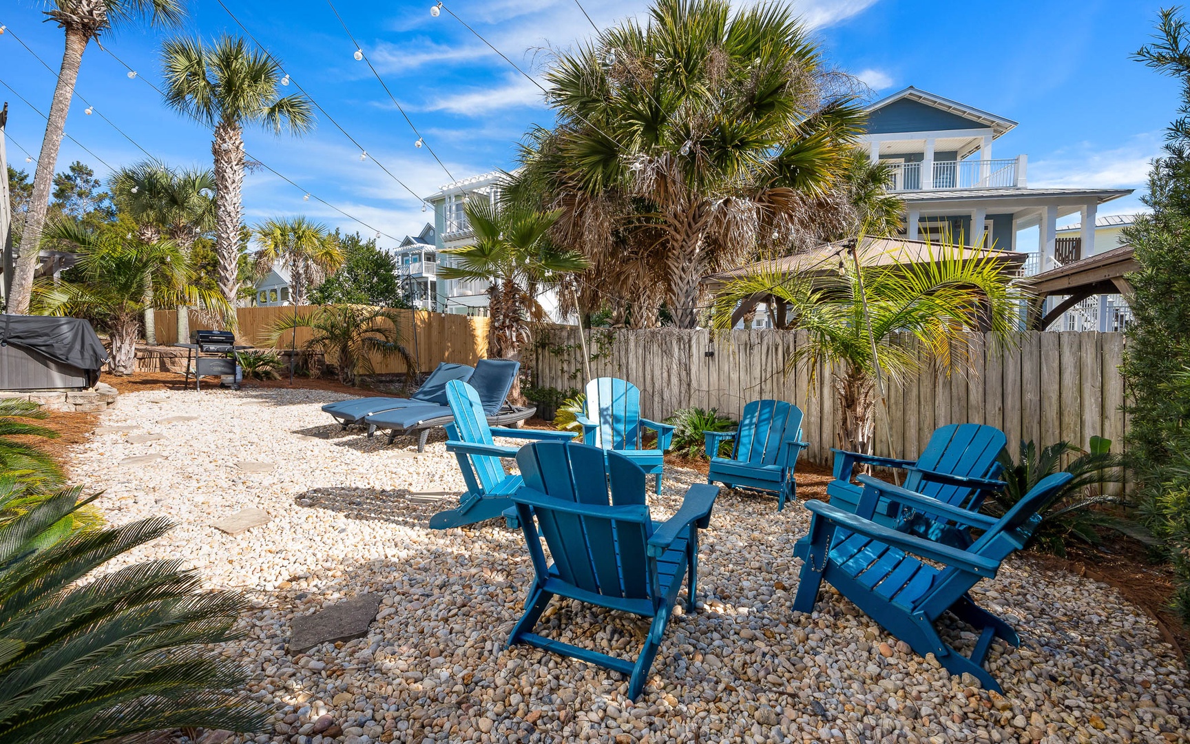 Relax in your private backyard oasis with vibrant blue Adirondack chairs, tropical palms, and string lights for magical evenings under the stars.
