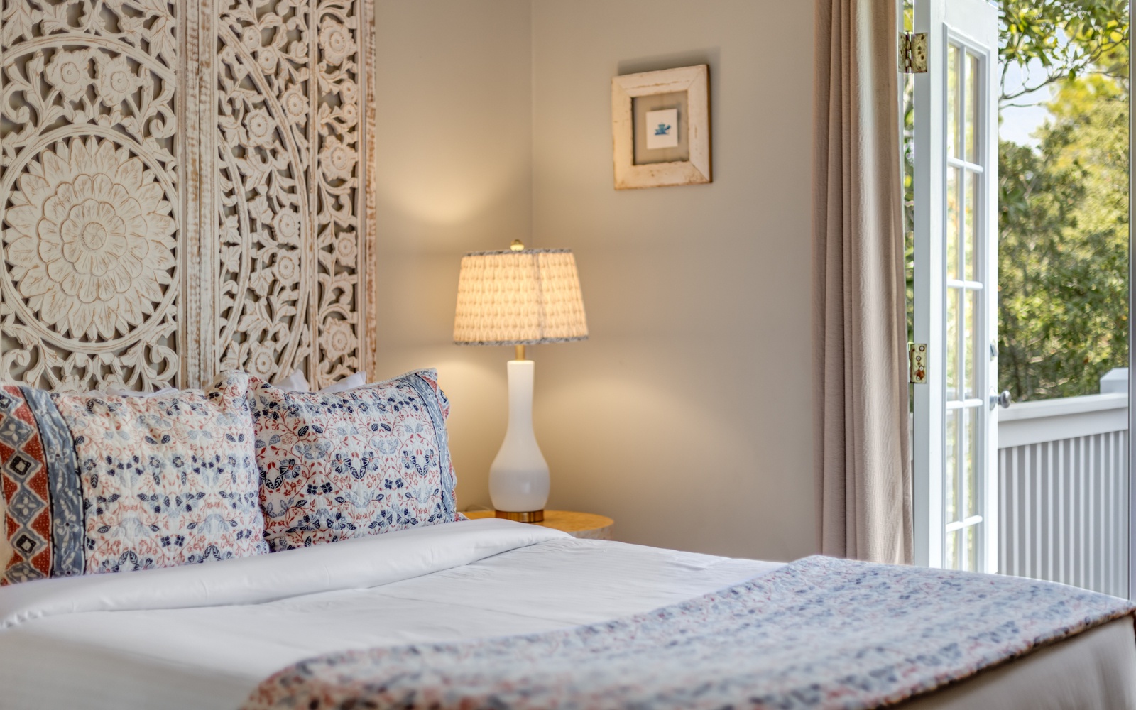 Drift off to sleep in your cozy bedroom adorned with intricate carved panels and patterned linens, while gentle daylight filters through your private balcony doors.