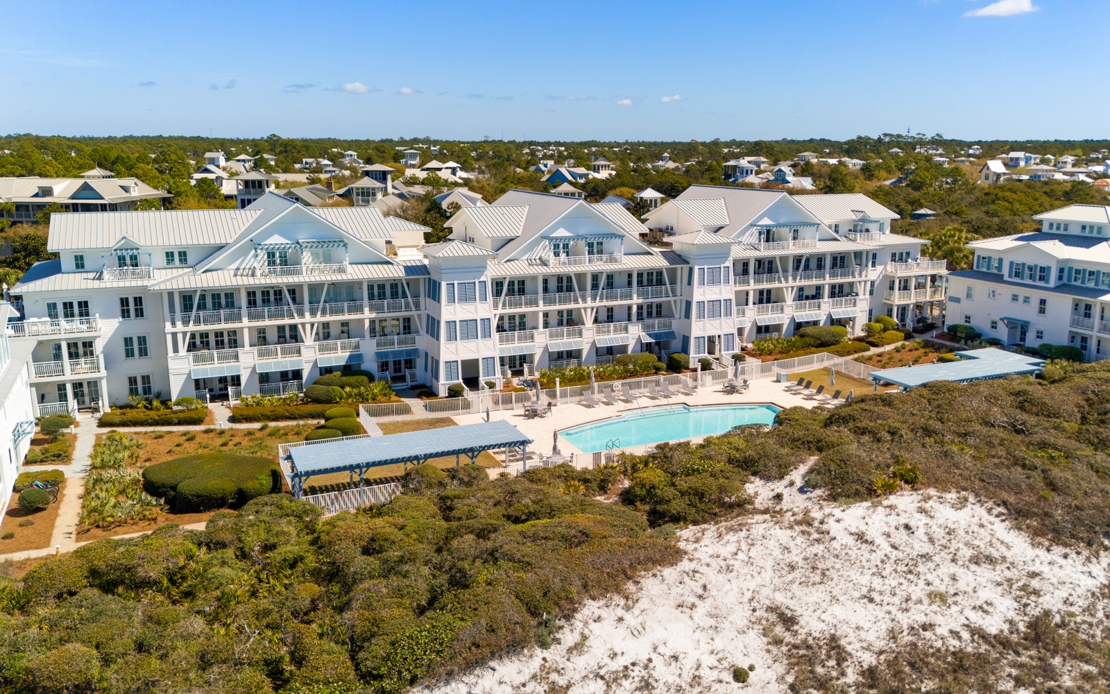 Coastal resort community featuring multiple buildings with pool and natural dunes nearby.