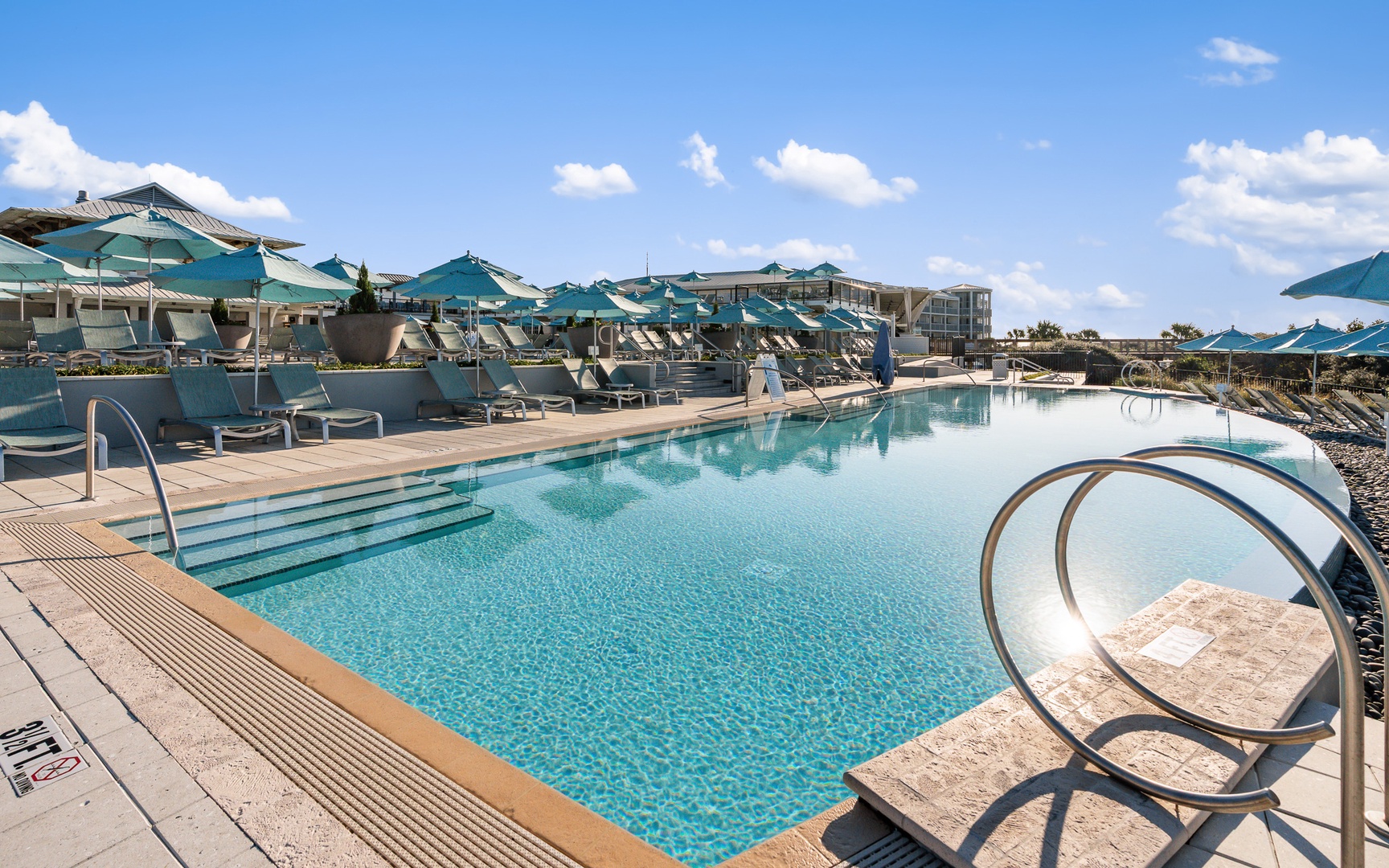 Resort-style pool deck with turquoise umbrellas and comfortable loungers under sunny skies.