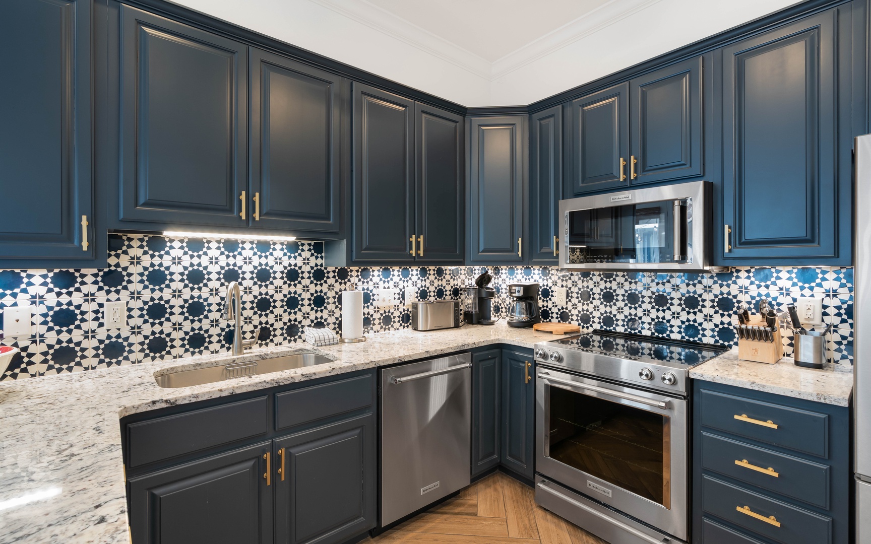 Your stylish kitchen features navy cabinetry, marble countertops, and stunning patterned tile backsplash, fully equipped for cooking memorable meals.