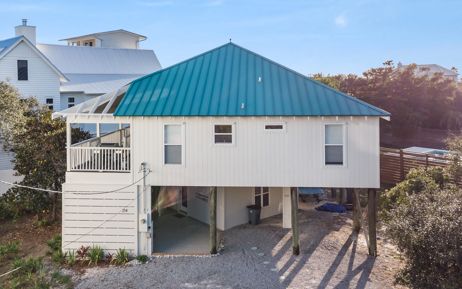 Coastal vacation home with distinctive teal roof and elevated design, featuring covered parking and deck space in a peaceful neighborhood setting.